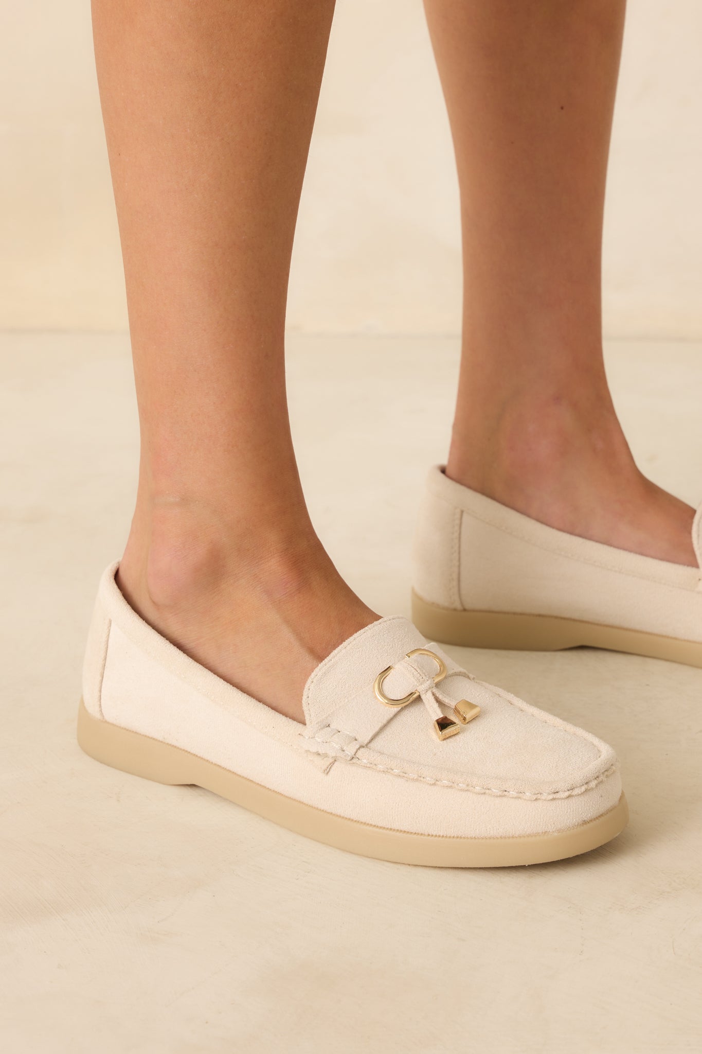 Cropped side view of the ivory penny loafers highlighting the faux suede texture, saddle strap, and gold charm detailing.