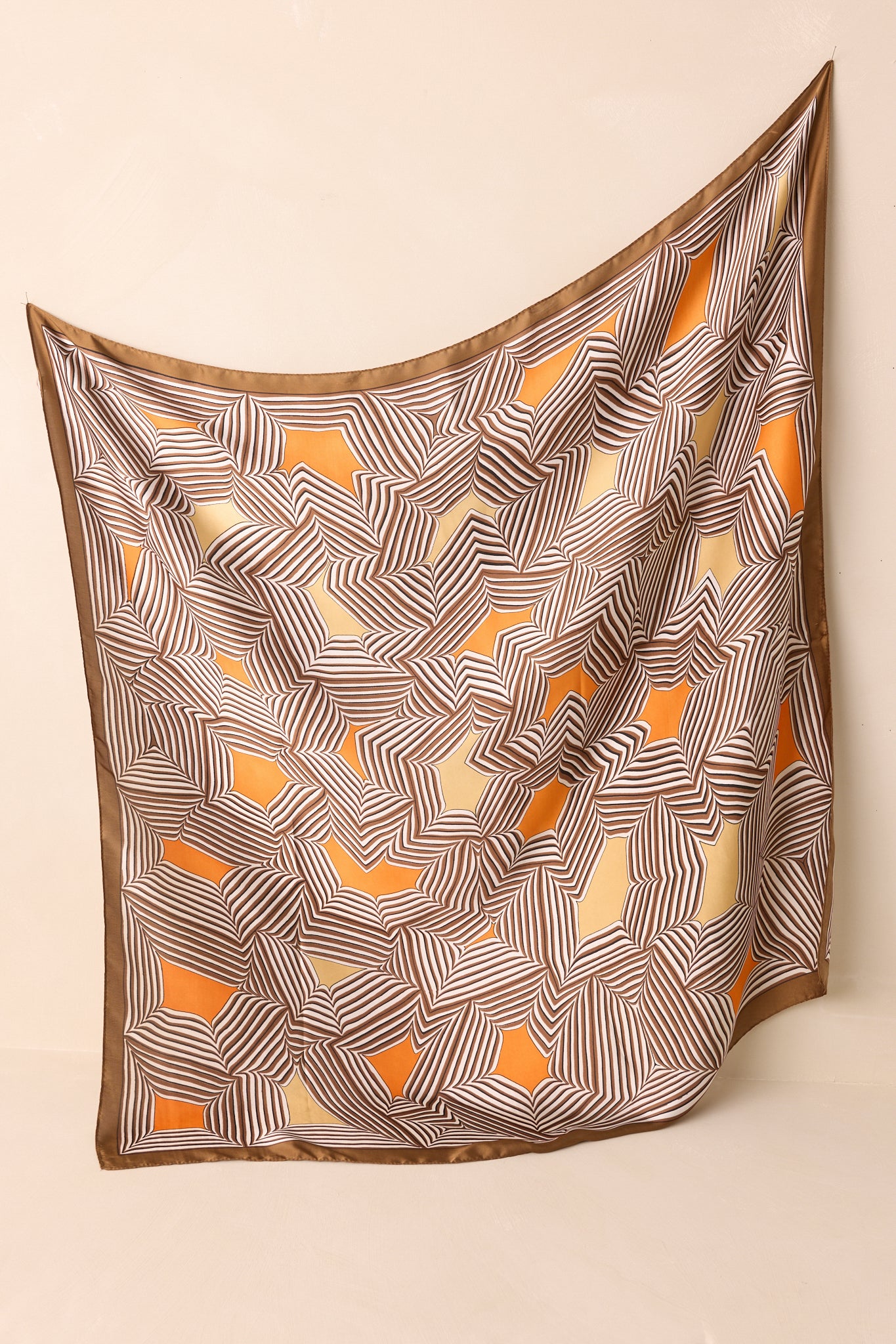 Full view of the large brown scarf laid flat, featuring a stripe geometric print with orange and golden yellow accents and a shiny satin finish.