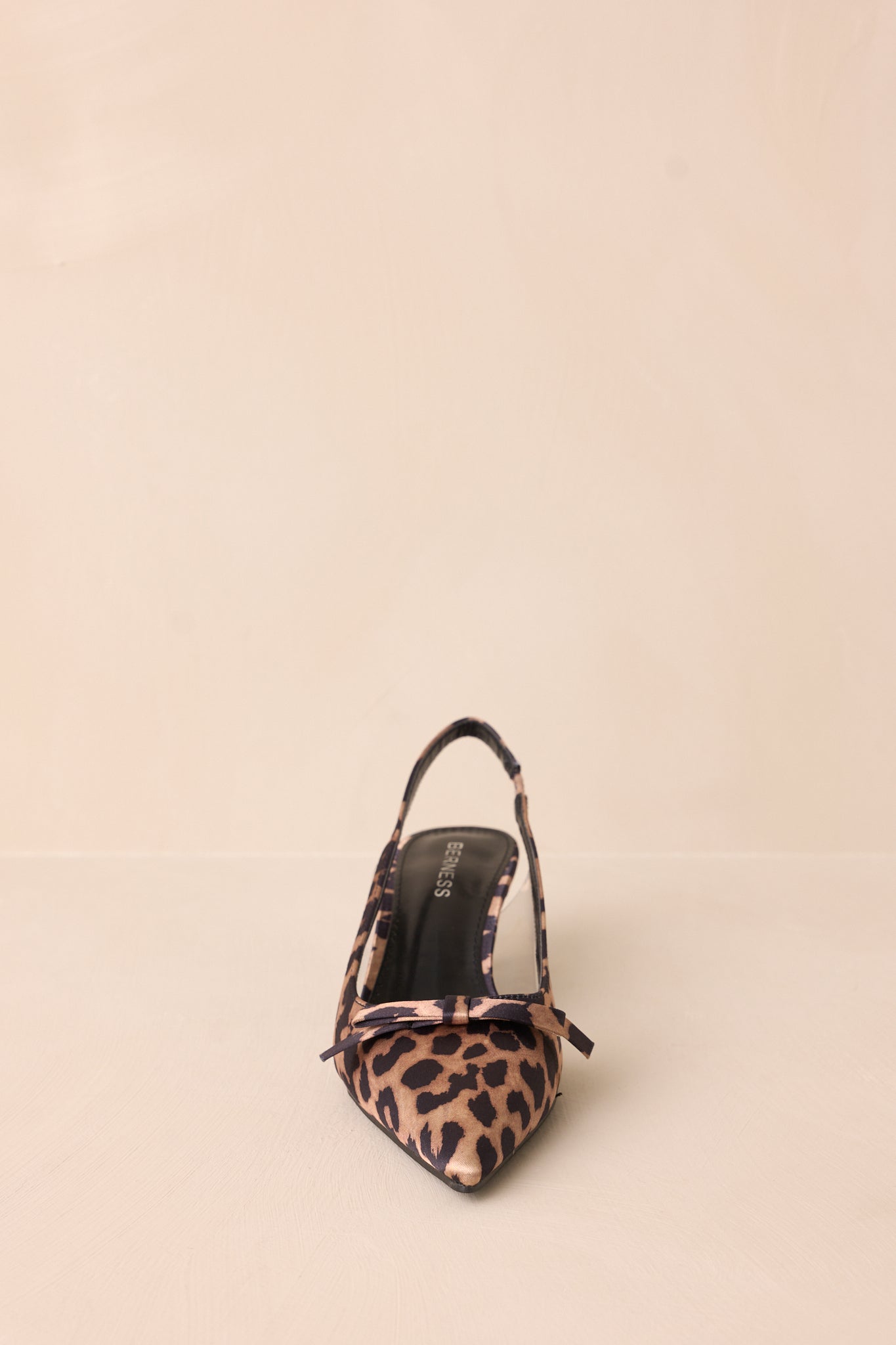 Front view of leopard kitten heels featuring a pointed closed toe, delicate bow detailing, a strap around the back of the foot, clear siding for extra support, and an extremely short heel.