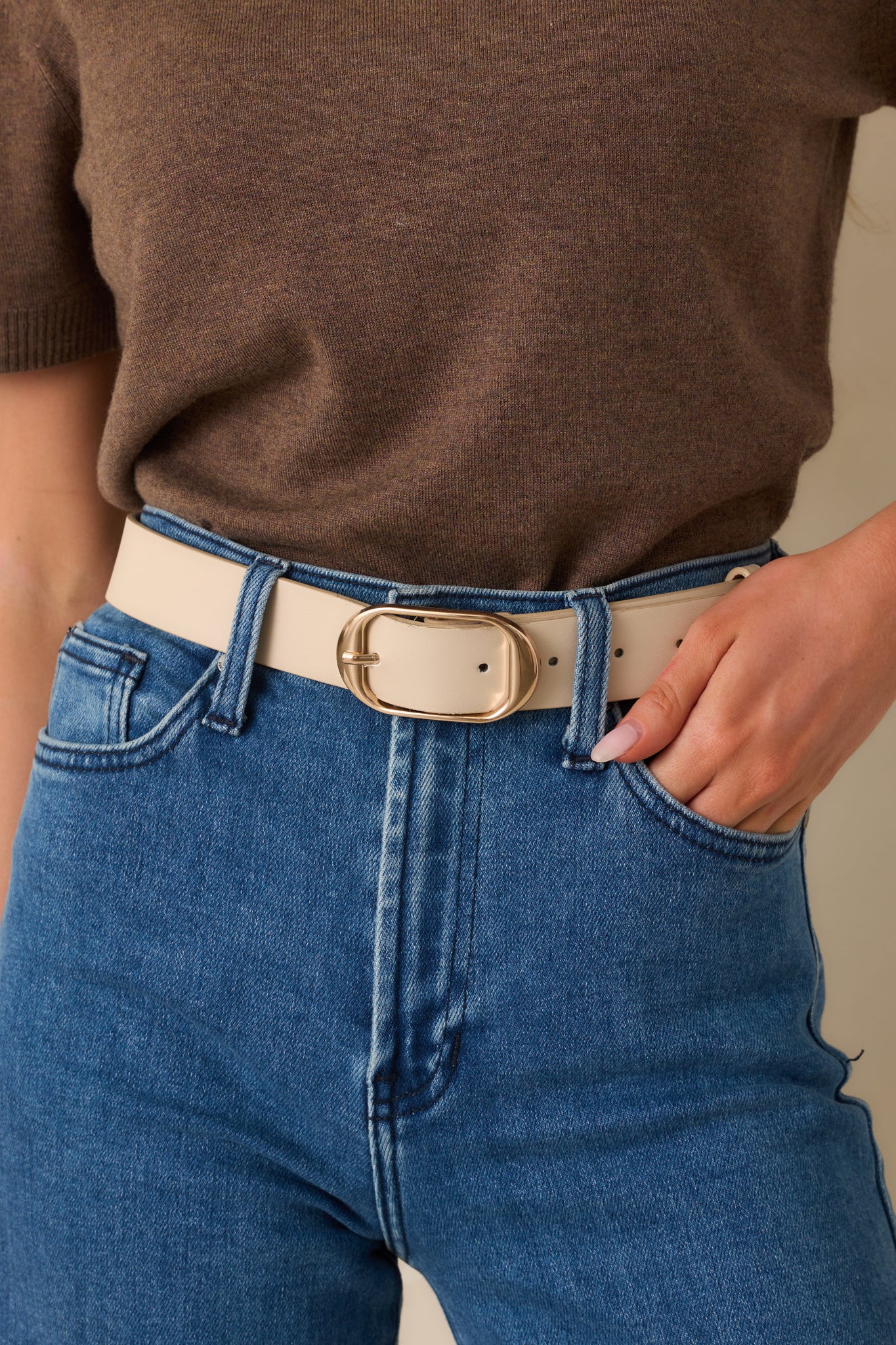 Cropped front view of the light taupe belt showing the thick, smooth material and shiny gold rounded buckle.