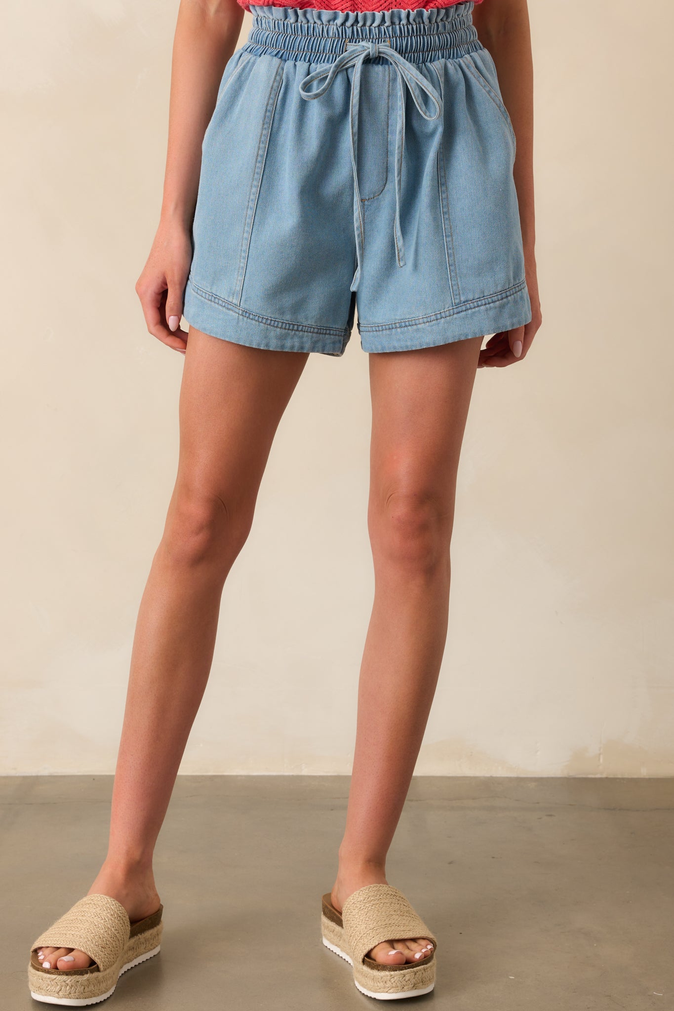 Cropped view of light wash shorts showing the ruffle edge along the waistband and adjustable drawstring.