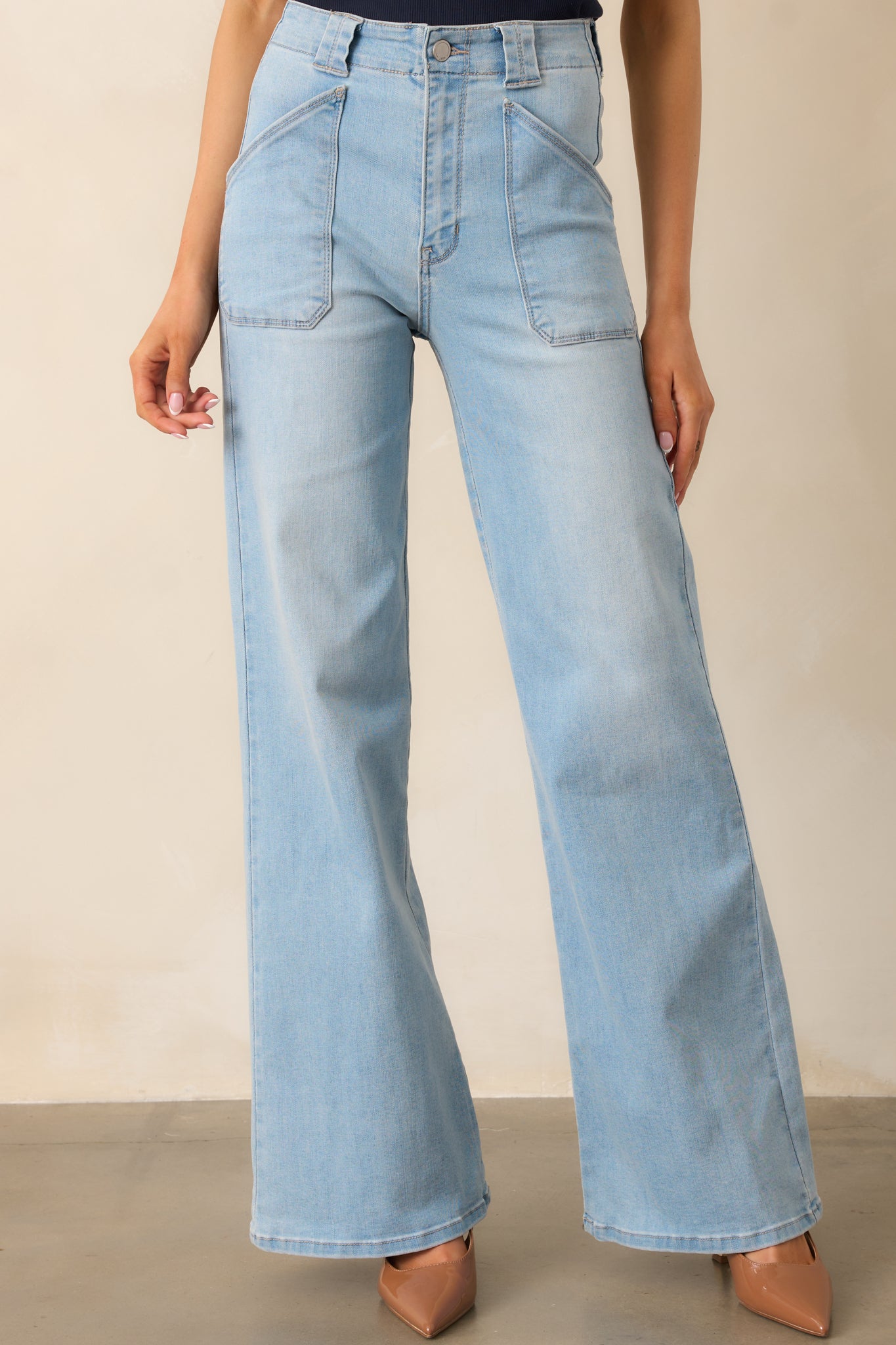 A closer look at the light wash high-waisted jeans, showcasing the structured waistband, belt loops, and functional front patch pockets.