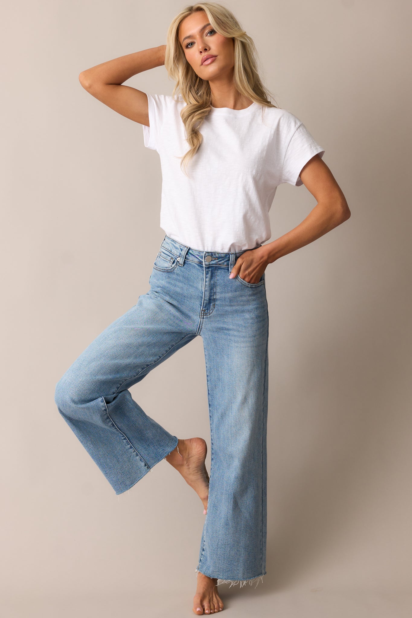 A stylish pair of light wash jeans with a raw hem, wide leg silhouette, and classic button and zipper closure.