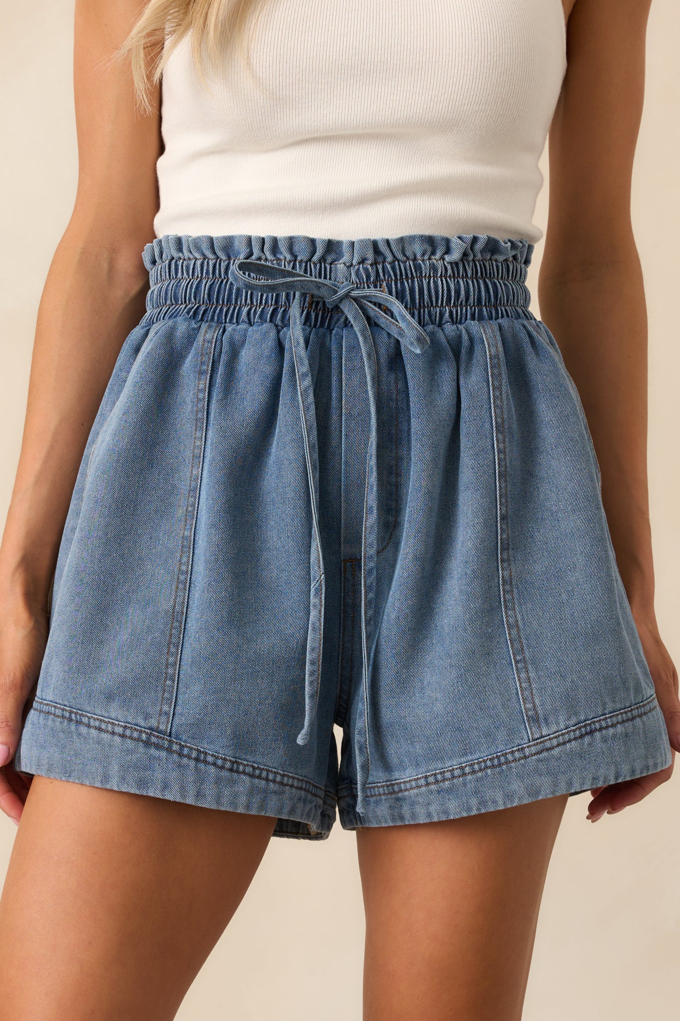 lose-up of ruffle trim, drawstring tie, and gathered waistband on medium wash denim shorts.