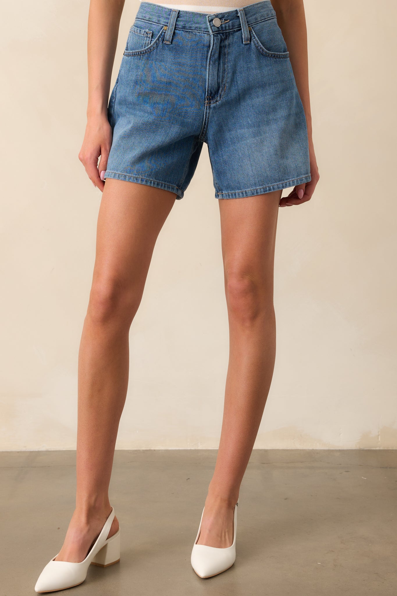A detailed view of the jean shorts shows the clean medium wash 100% cotton denim, with visible functional pockets and the classic high-waisted fit, perfect for any casual look.