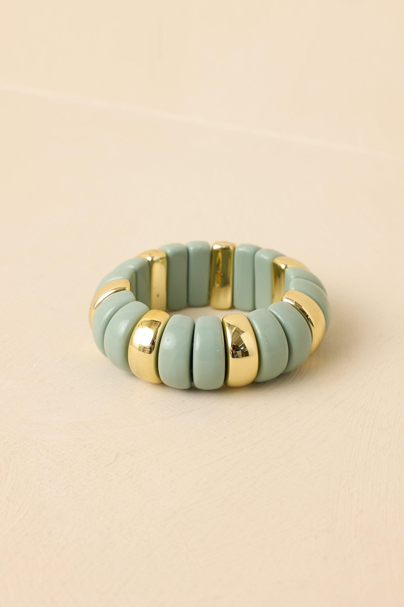 Pastel mint green stretch bracelet featuring glossy enamel disc beads with polished gold accents, photographed at a slightly elevated angle.