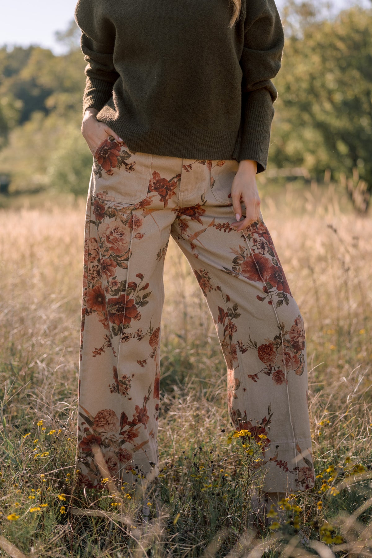 Model wearing taupe wide-leg pants with a rust floral print and front patch pockets, shown from the waist down.