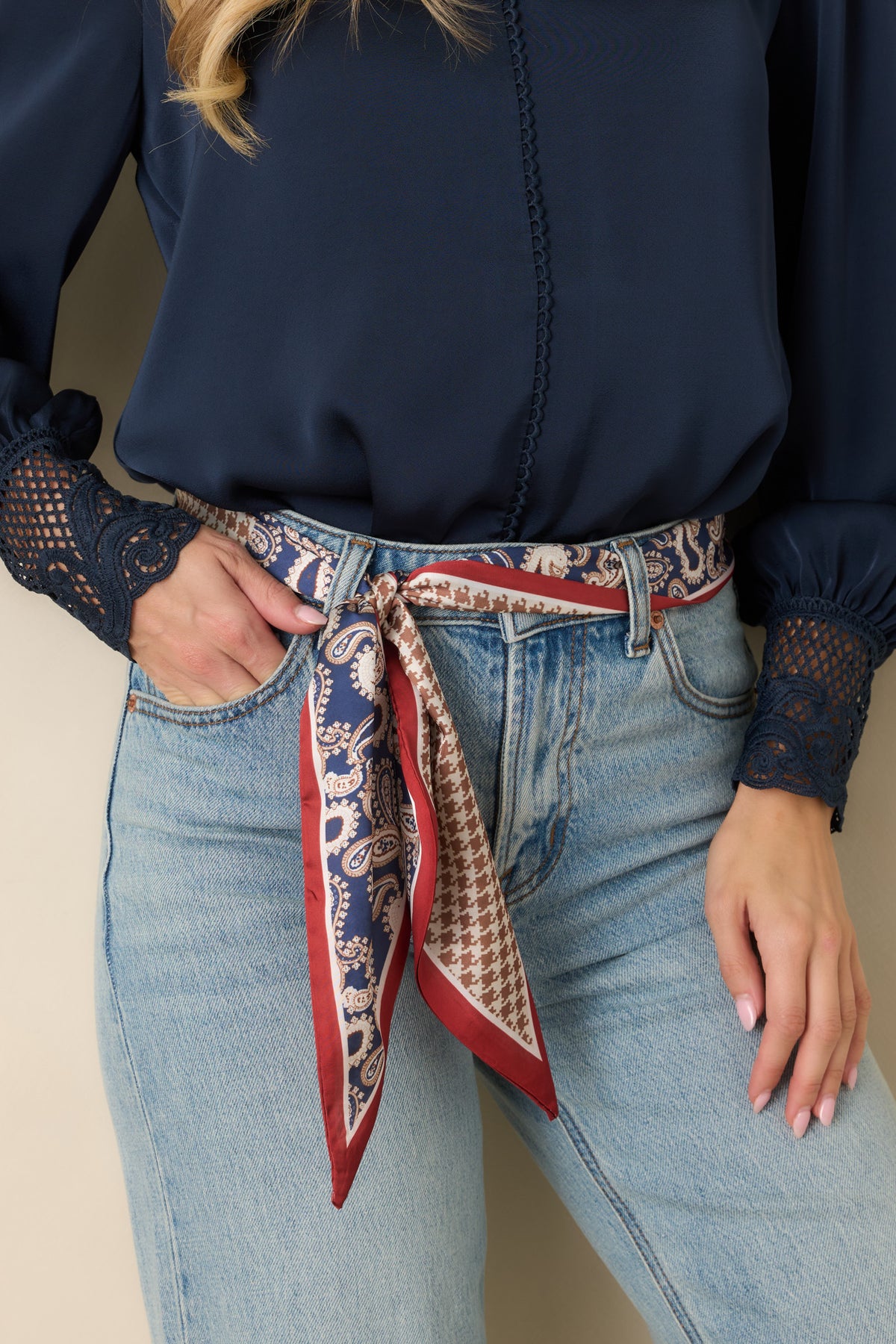 Close-up of a navy paisley and taupe houndstooth scarf with red borders, tied through jean belt loops.