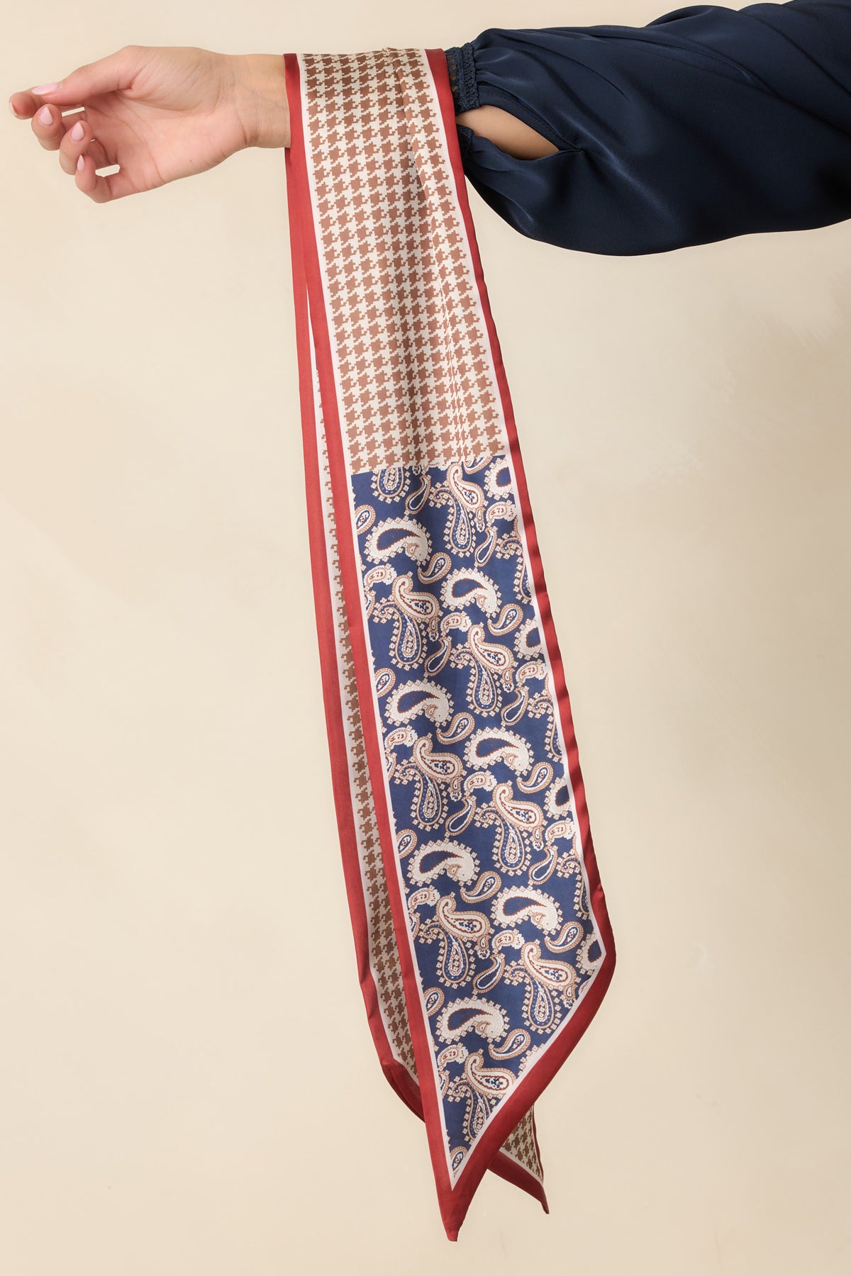 Navy paisley and taupe houndstooth scarf draped over an arm, showing red borders and pointed ends.