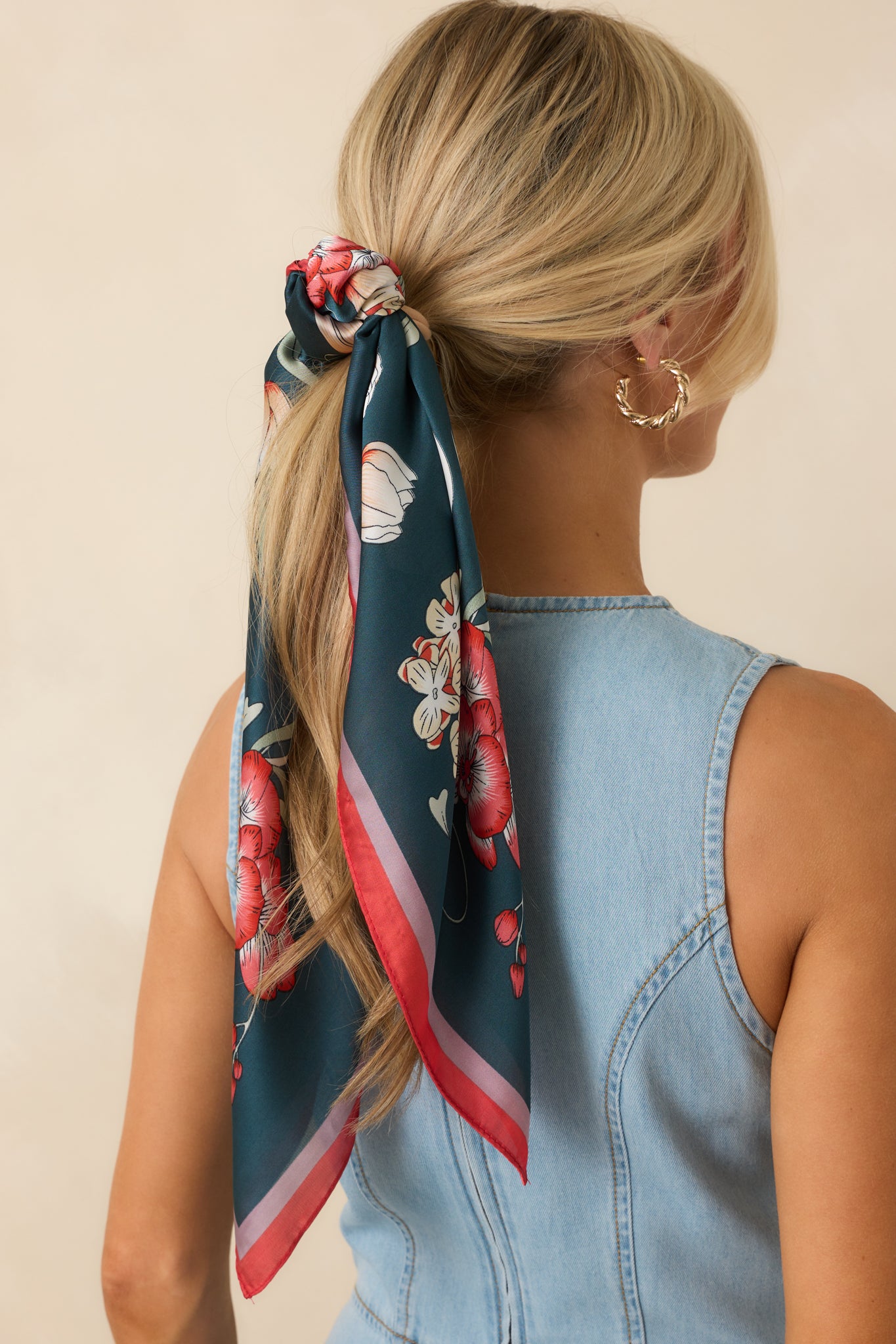 Back view of navy satin scarf tied around hair, highlighting red and pink border trim and floral design.