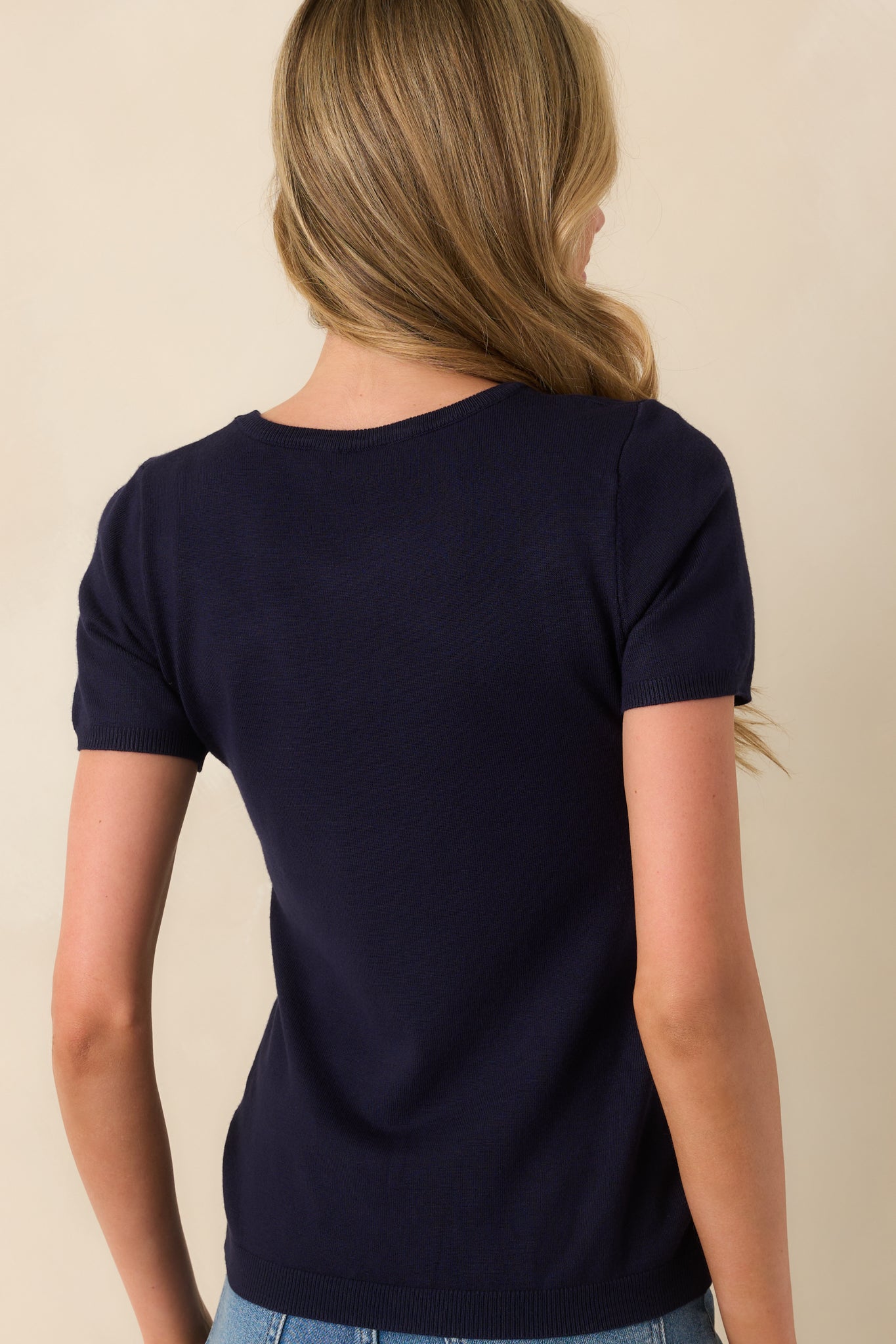 A back view of the navy sweater top displaying the short sleeves and consistent ribbed hem finish.