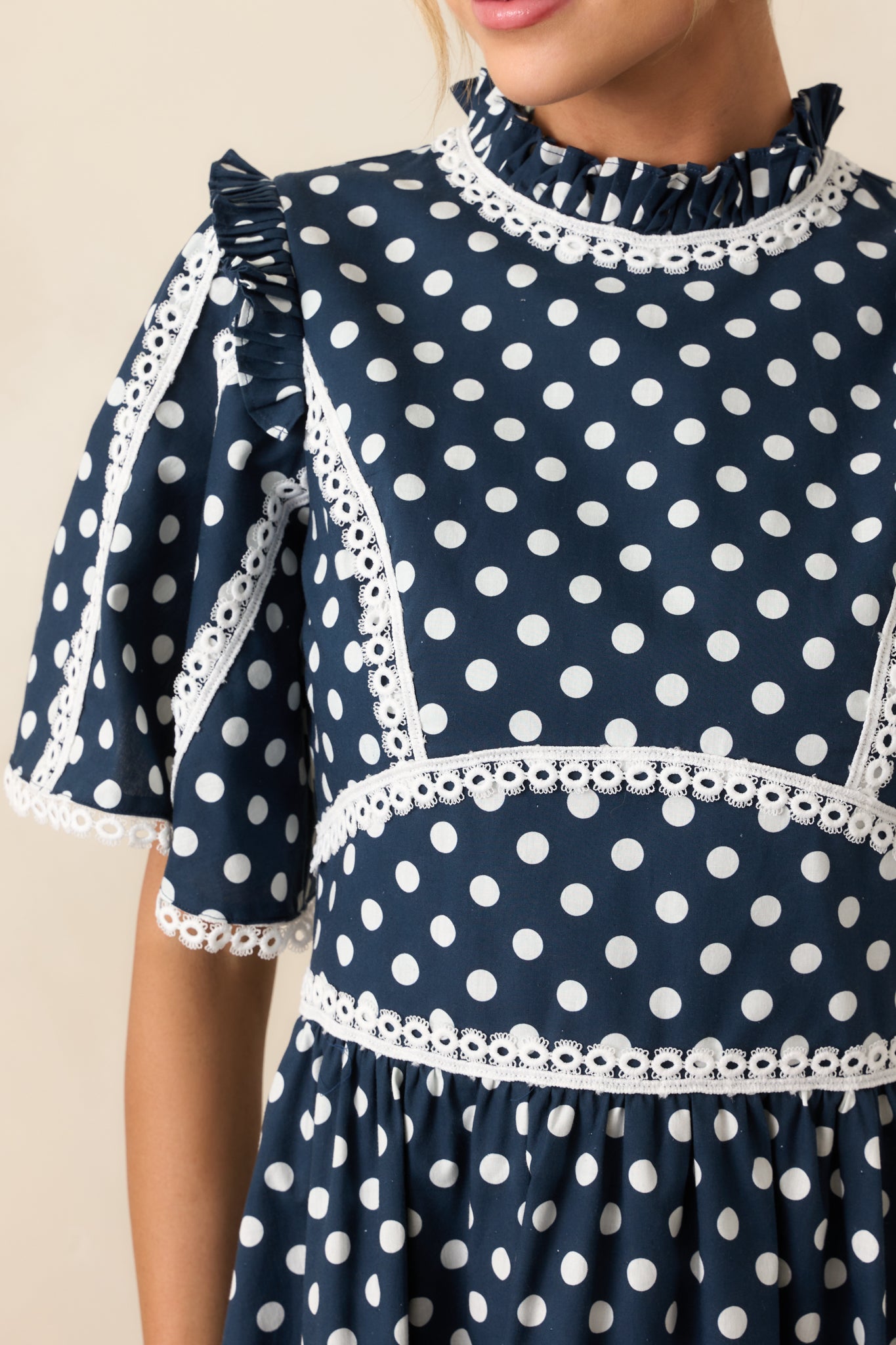 Detailed view of ruffle mock neckline and white eyelet trim on navy dress
