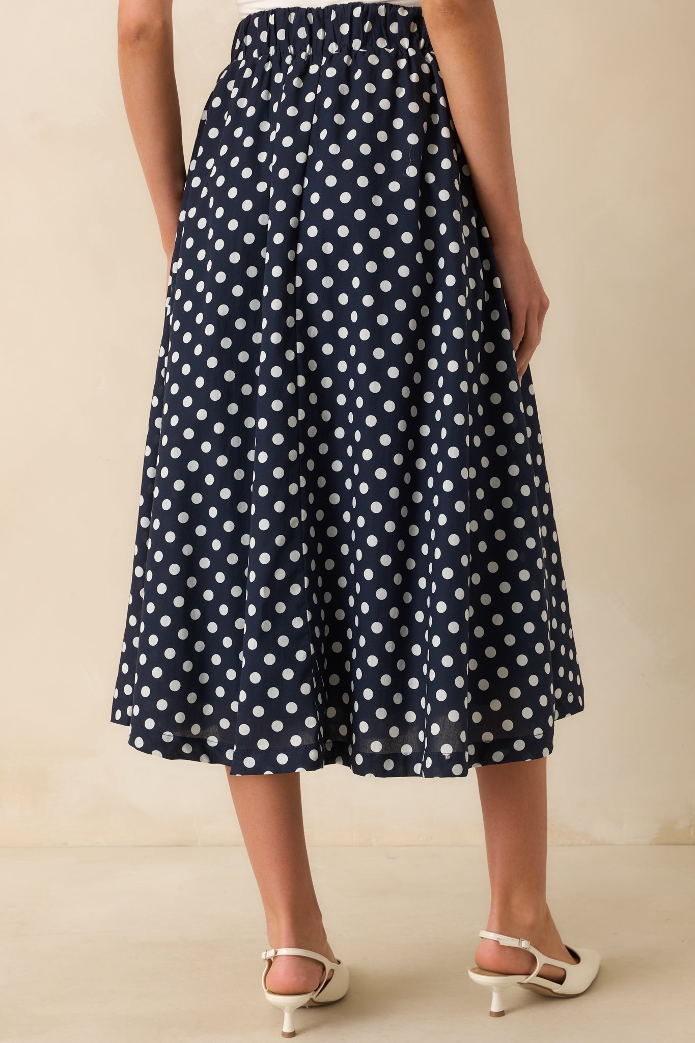Rear view of navy and white polka dot midi skirt showing elastic waist insert and smooth drape.