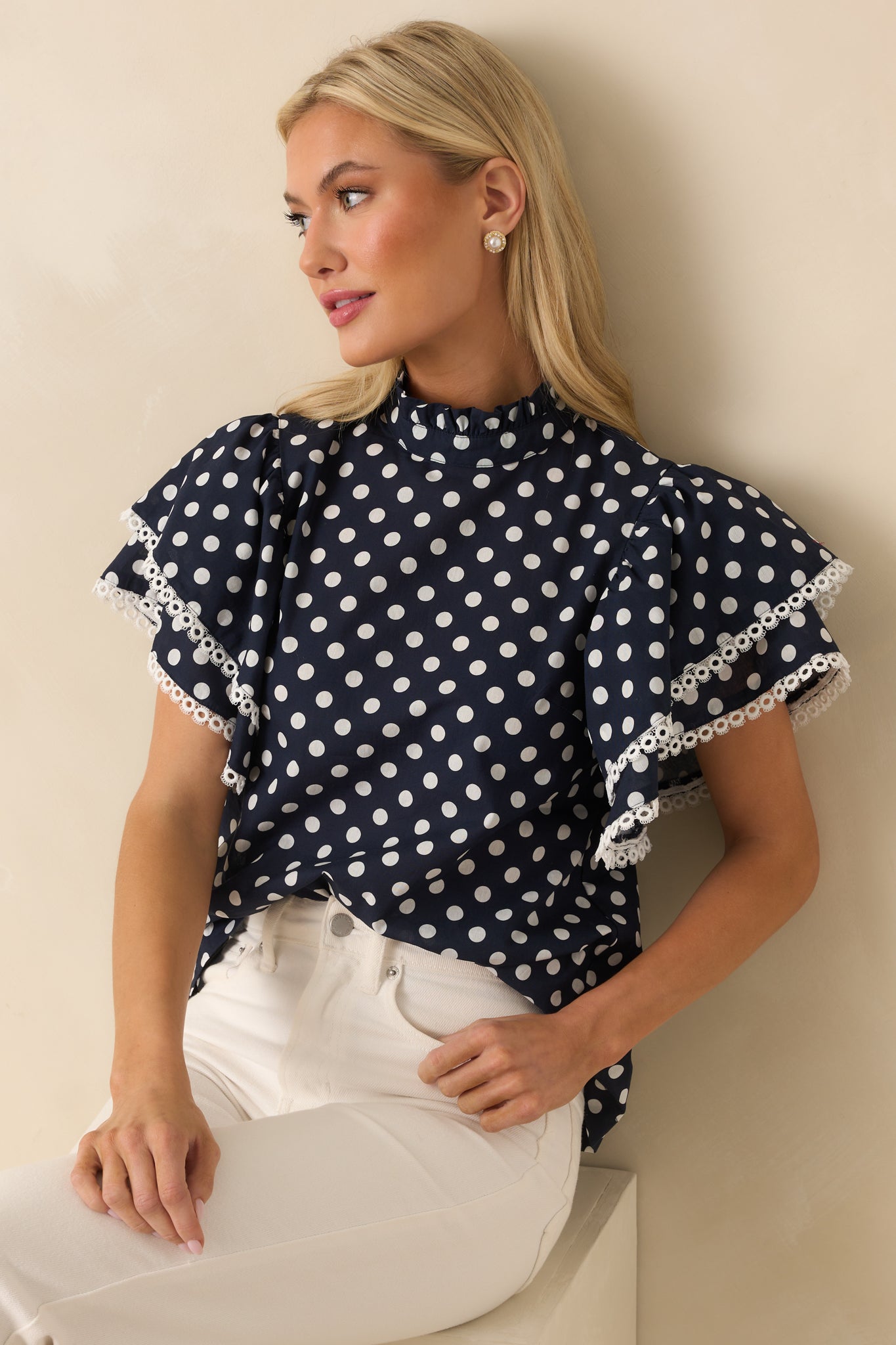 Relaxed fit navy polka dot top with delicate ruffle sleeves and a high mock neckline trimmed in ivory eyelet.