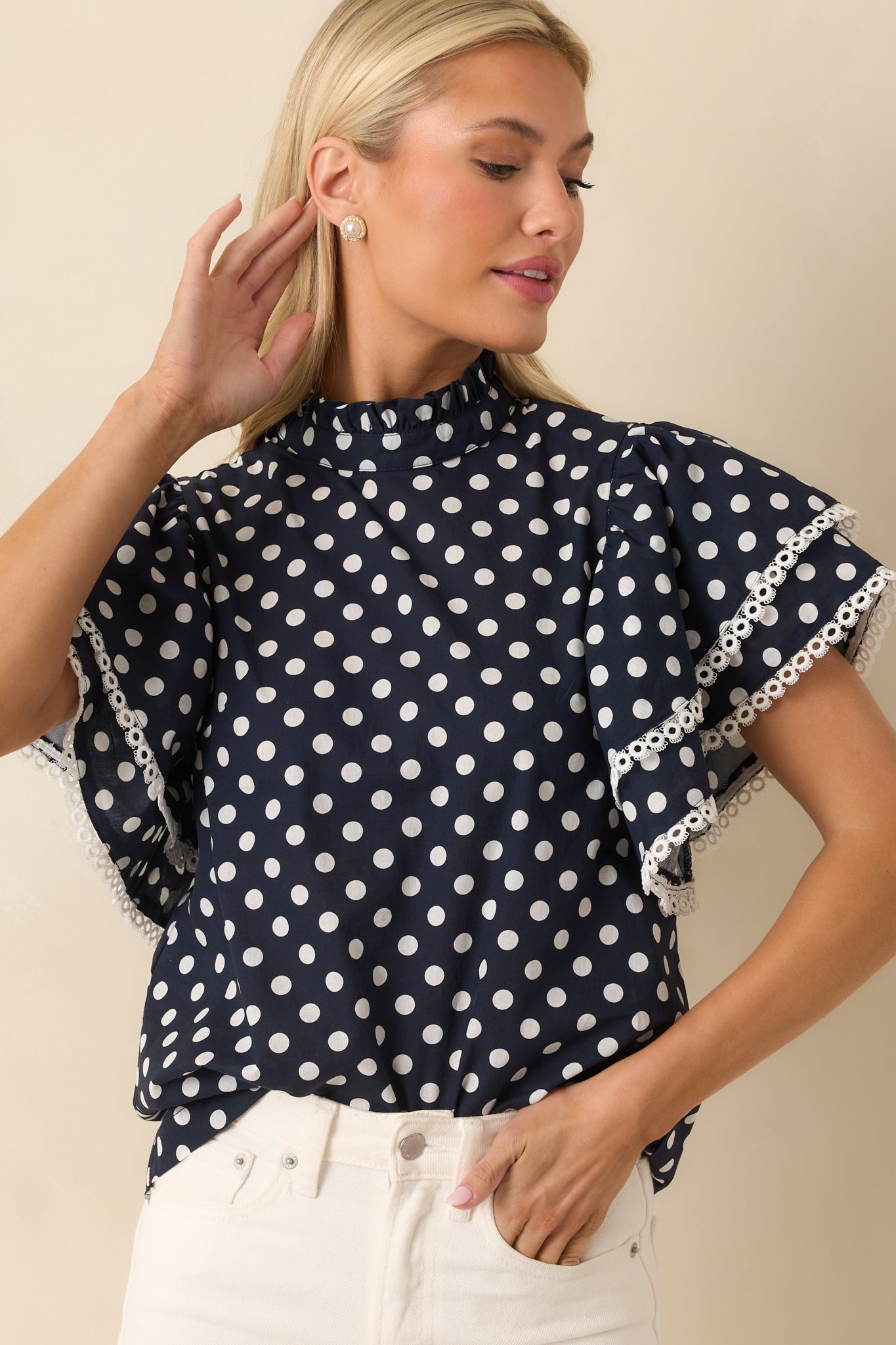 Detail of the short ruffle sleeve edge with ivory eyelet trim on a navy polka dot top.
