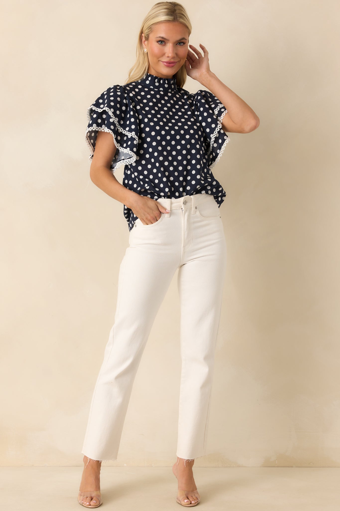 Lightweight polka dot top in navy and white with short ruffle sleeves and a ruffled mock neckline finished with ivory eyelet accents.