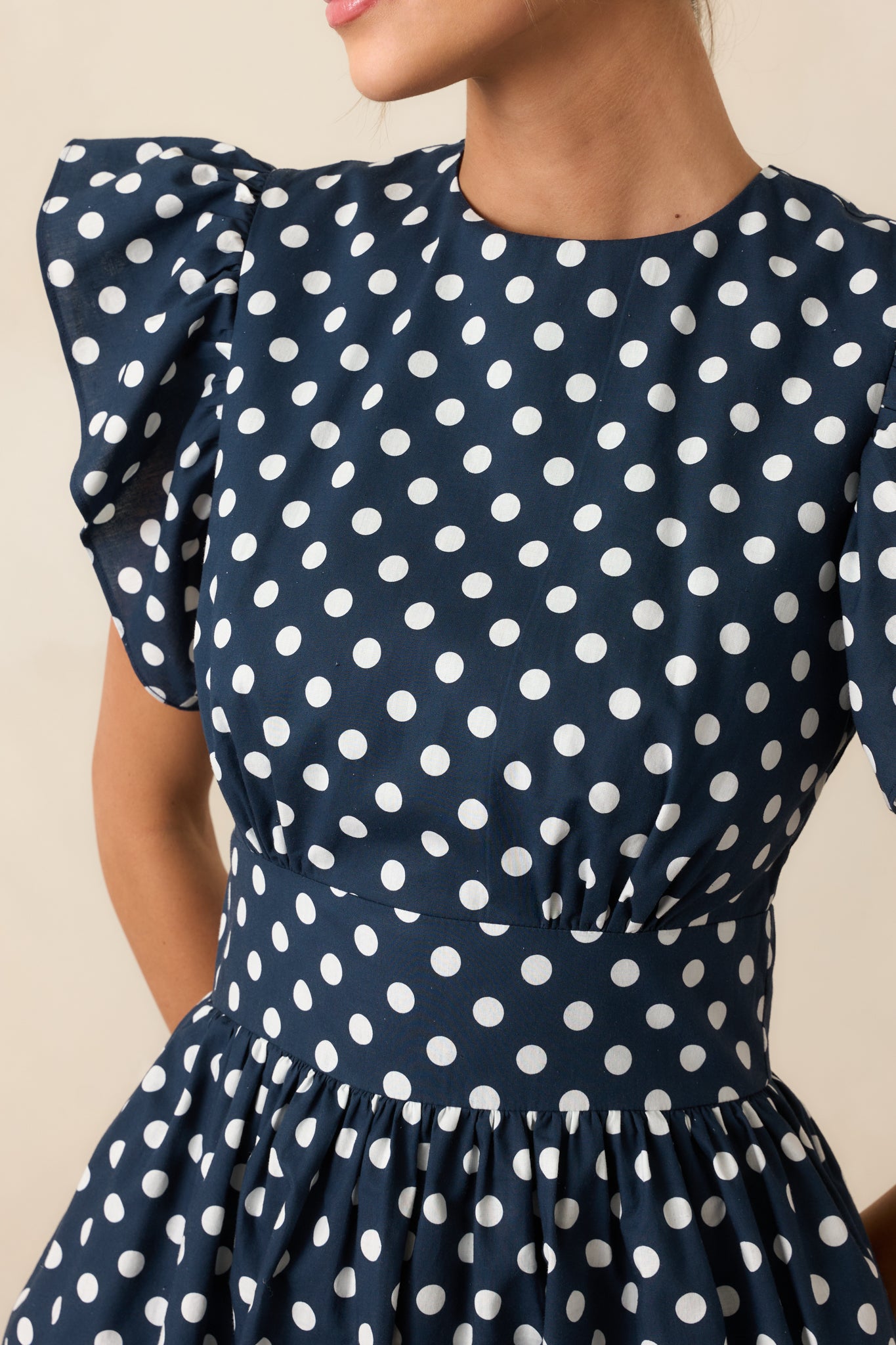 Close-up view of round neckline and flutter sleeve detail on polka dot maxi dress.