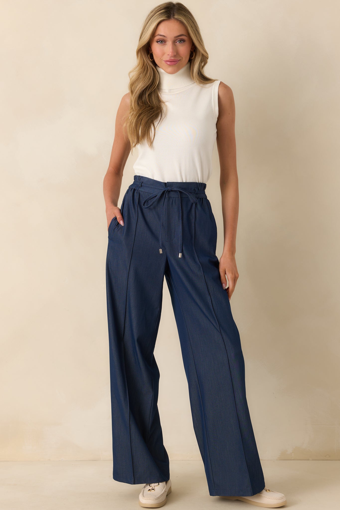 Front-facing full body view of the dark wash pants showing the high rise waist, slim silhouette, and functional front pockets.