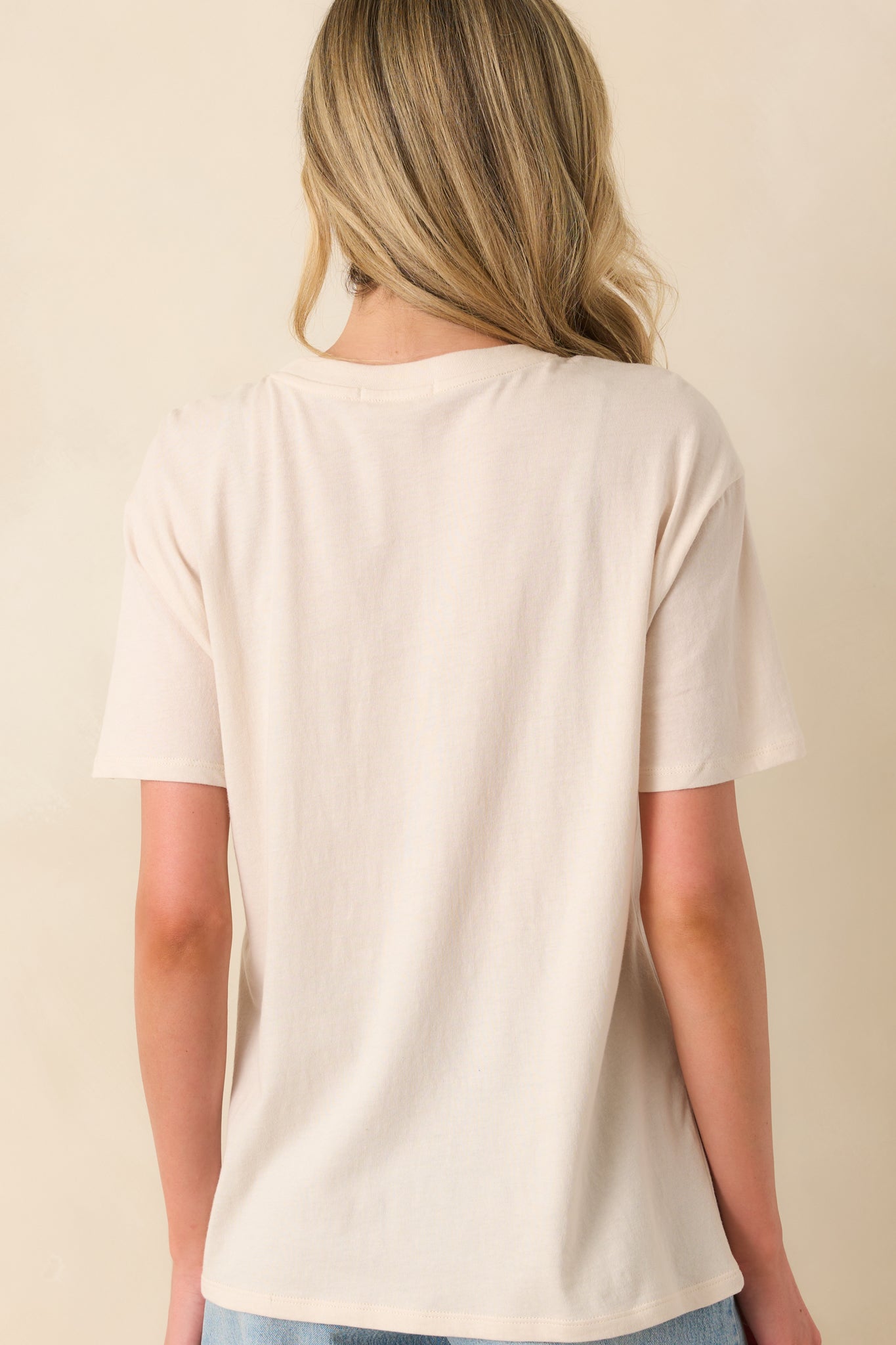 A view from behind of the light beige tee showing the relaxed fit, short sleeves, and plain back design.