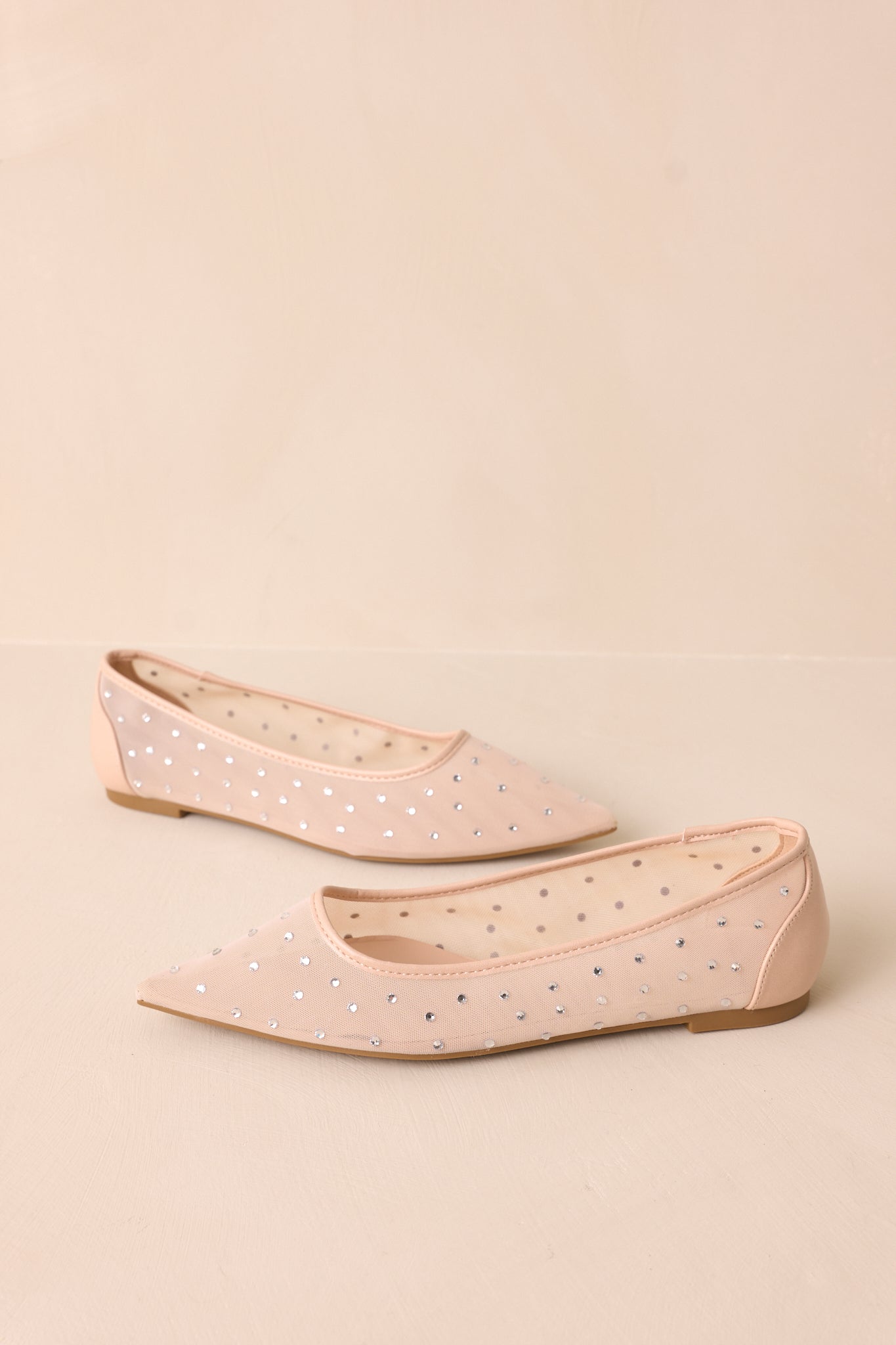 A side view of the flats, showcasing the beige trim along the rim and ankle piece with sparkling rhinestones.