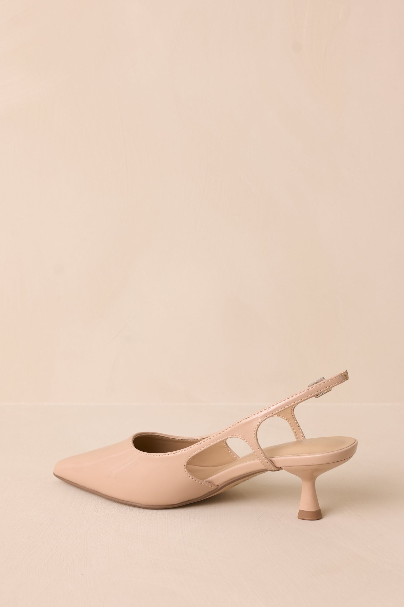Nude patent pointed heel with gold buckle detail and side cutout, inside side view.