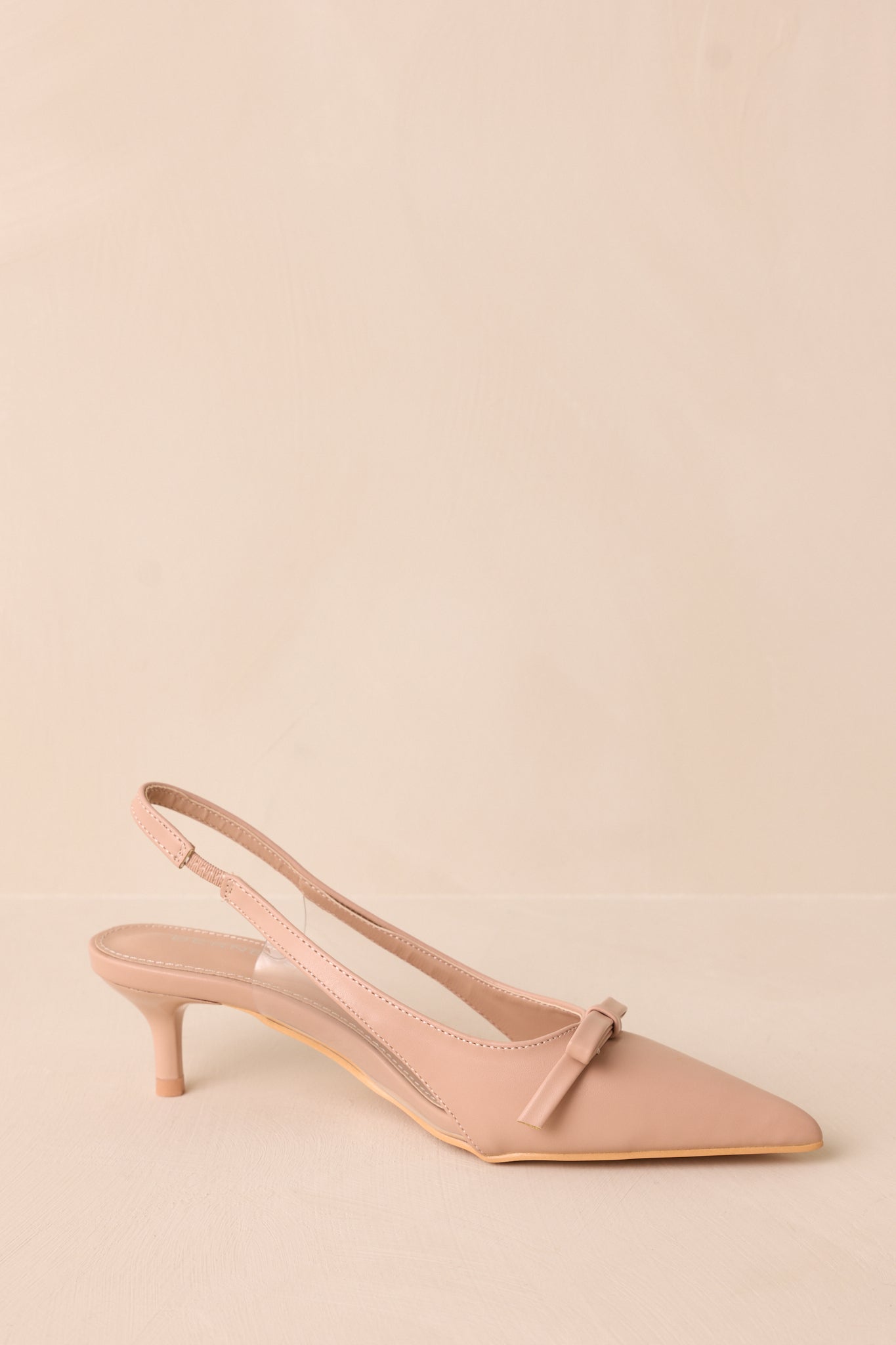 Angled back view of beige kitten heels highlighting the strap around the back of the foot and the extremely short heel.
