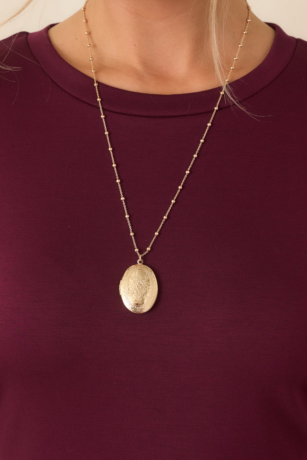 Close-up of the On Repeat Gold Locket Necklace showing the engraved oval pendant and beaded chain.