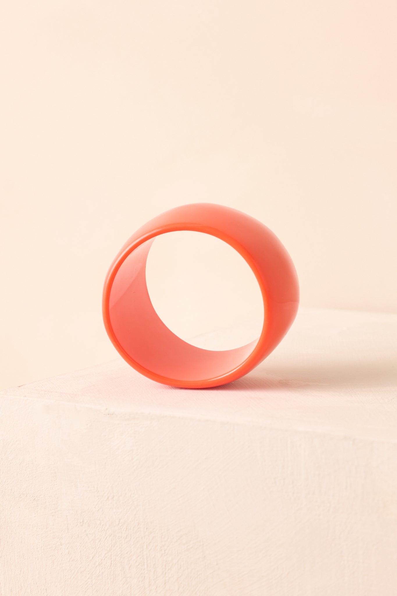 Orange sculptural bangle displayed on beige background with sleek, polished shine.