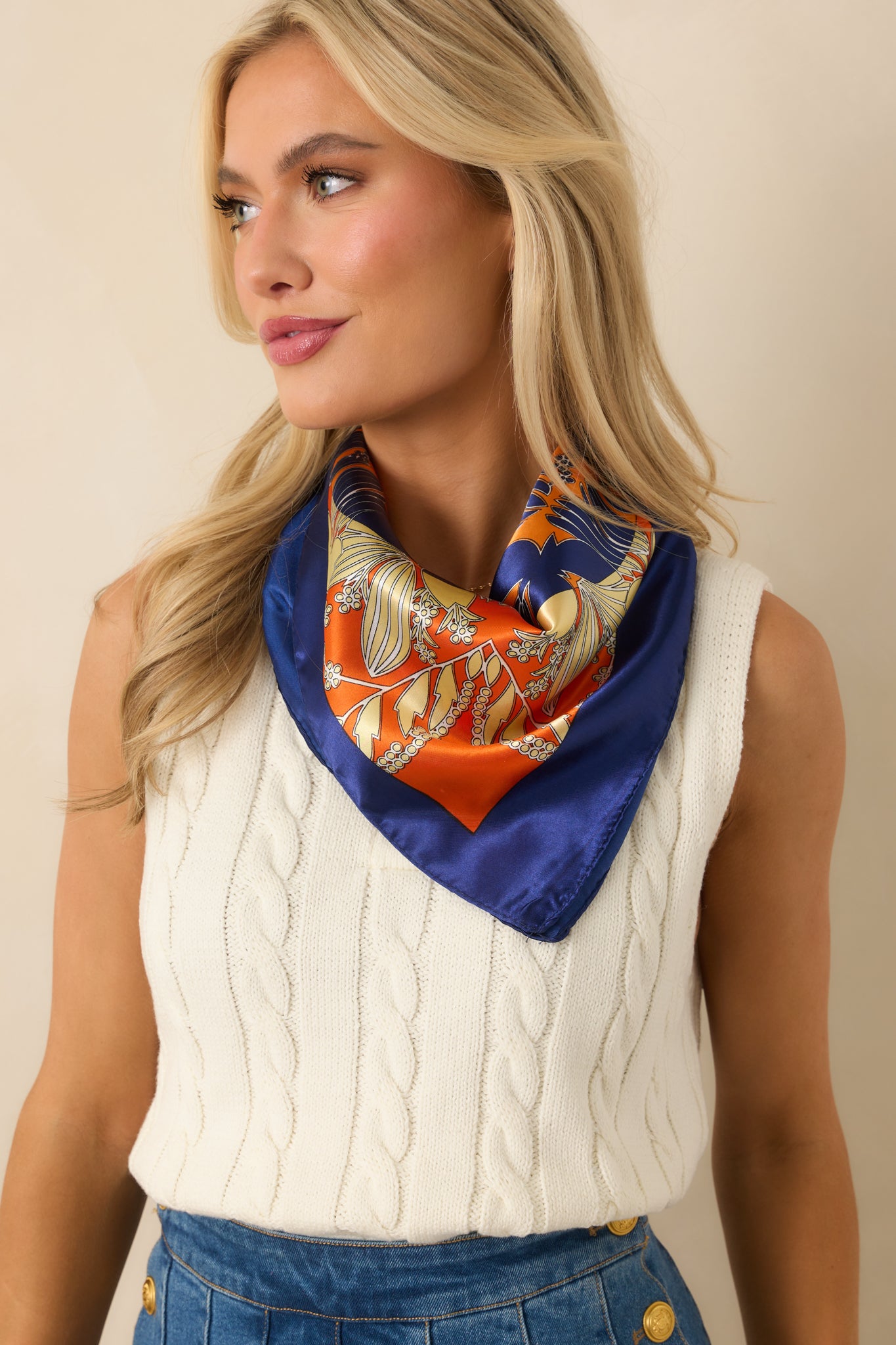 Orange square scarf with multicolor floral geometric print and four-leaf clover motif, styled neatly around the neck.