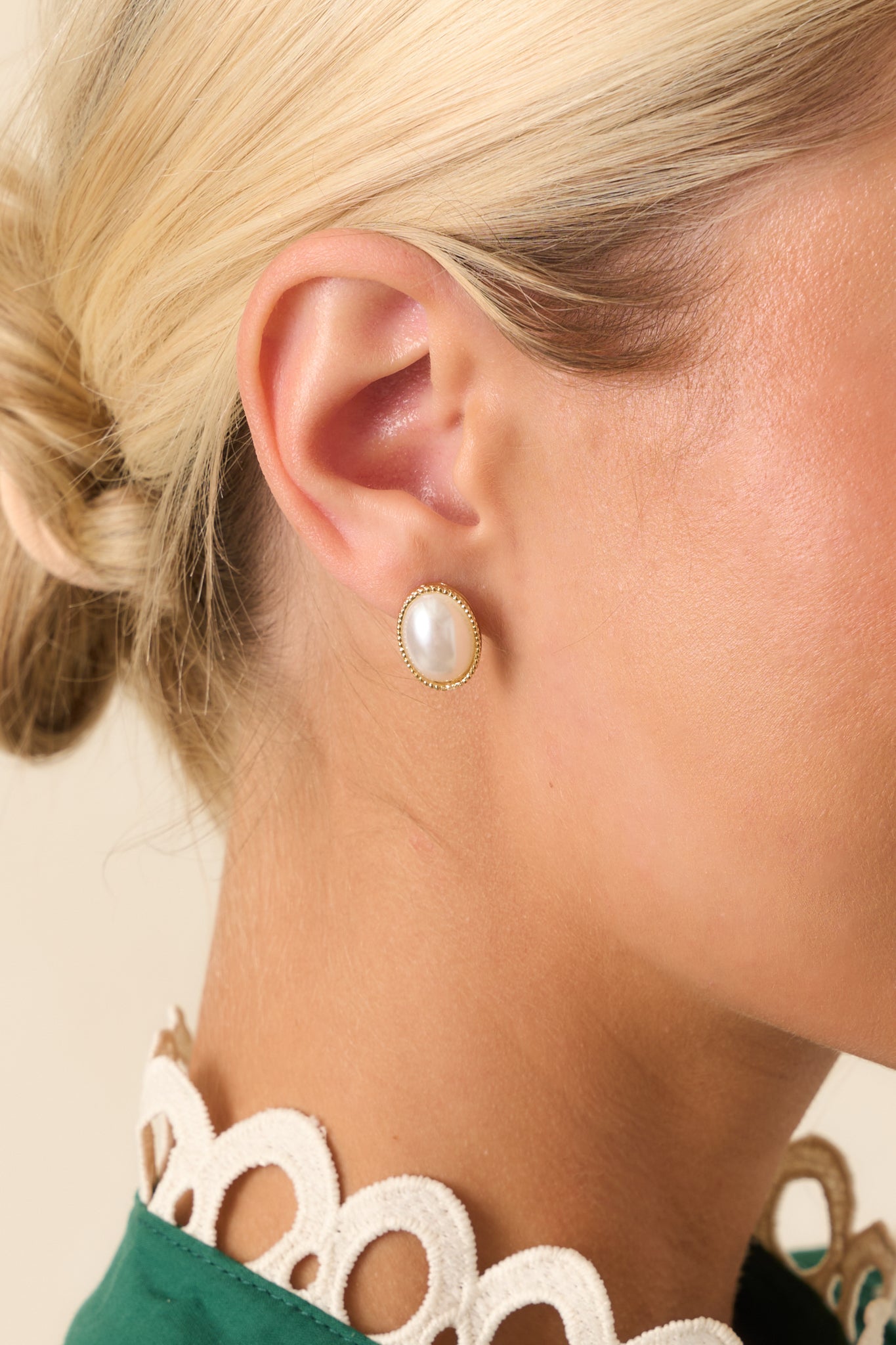 A close-up detail of one earring showing the intricate gold texture encircling the smooth, oval faux pearl centerpiece.