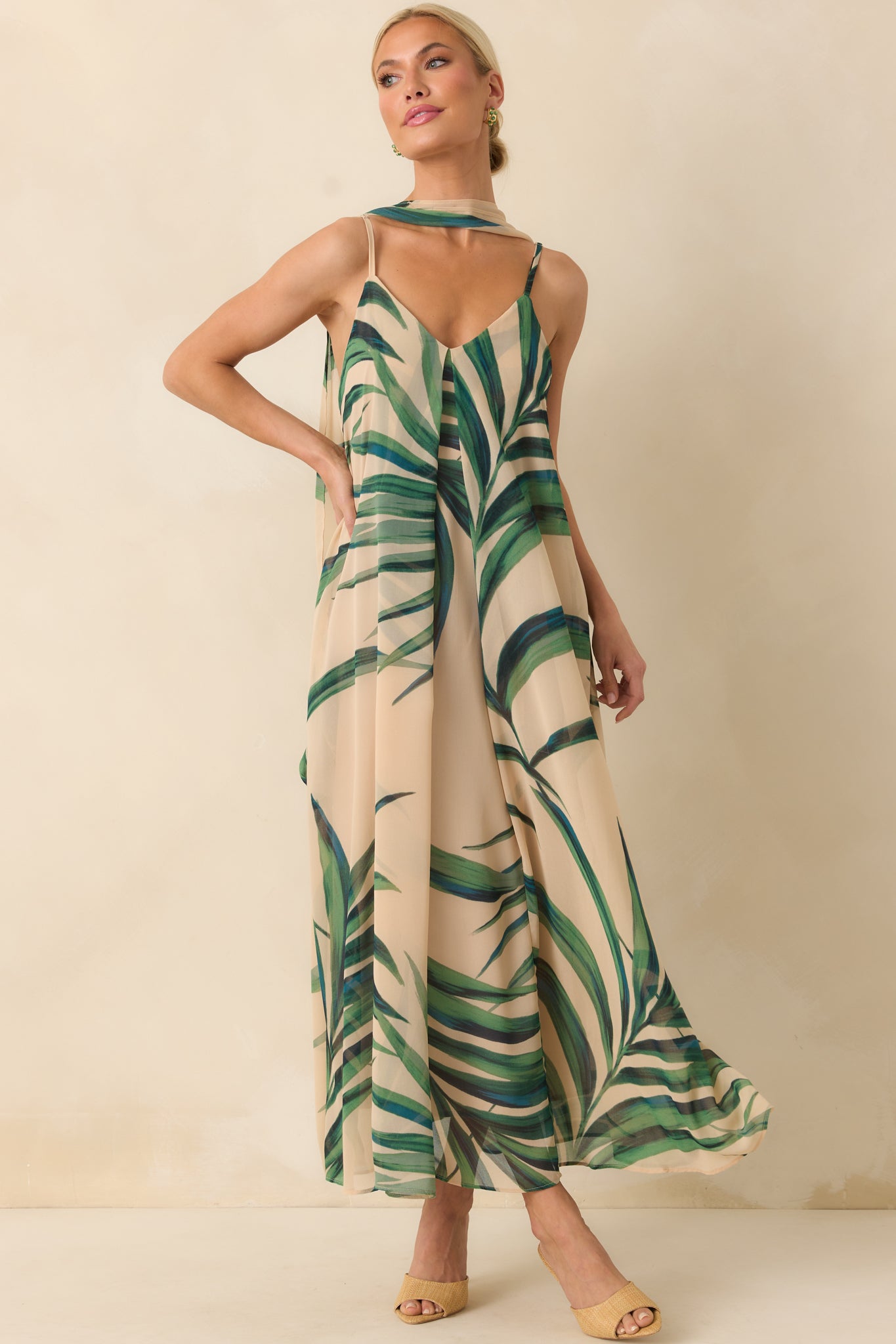 Full body photo of model wearing a beige maxi dress that features a green palm print chiffon overlay and shows the optional self-tie belt as a neck scarf.
