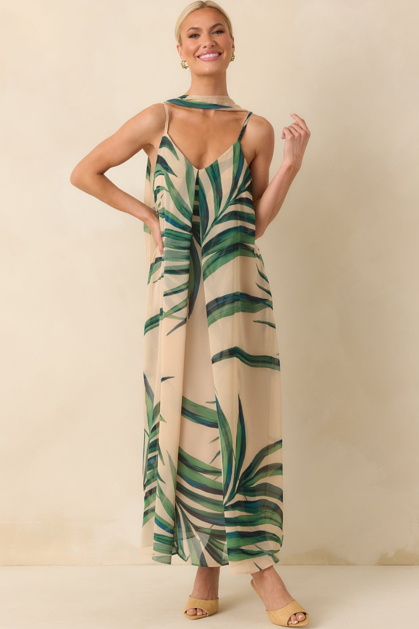 Full body photo of model wearing a beige maxi dress that features a green palm print chiffon overlay and shows the optional self-tie belt as a neck scarf.