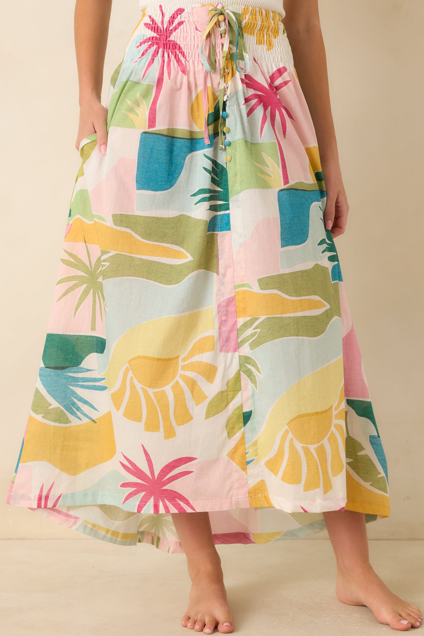 Alternate front view of the Paradisa tropical print maxi skirt featuring a smocked waistband, adjustable tie waist, side pockets, and a pastel tropical landscape print.