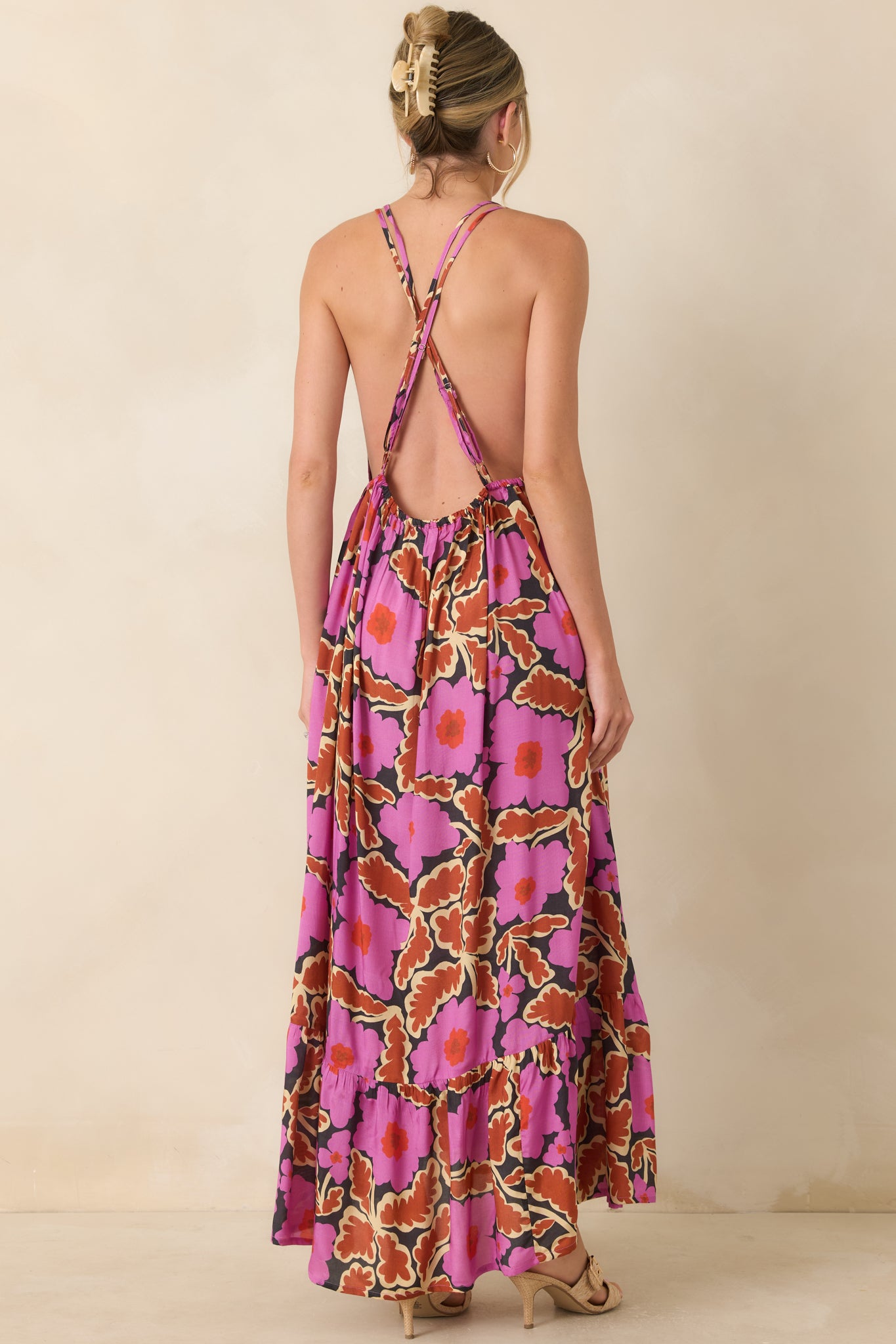 Back view of a pink and brown floral maxi dress featuring an open back, adjustable crisscross straps, and a flowy tiered skirt.