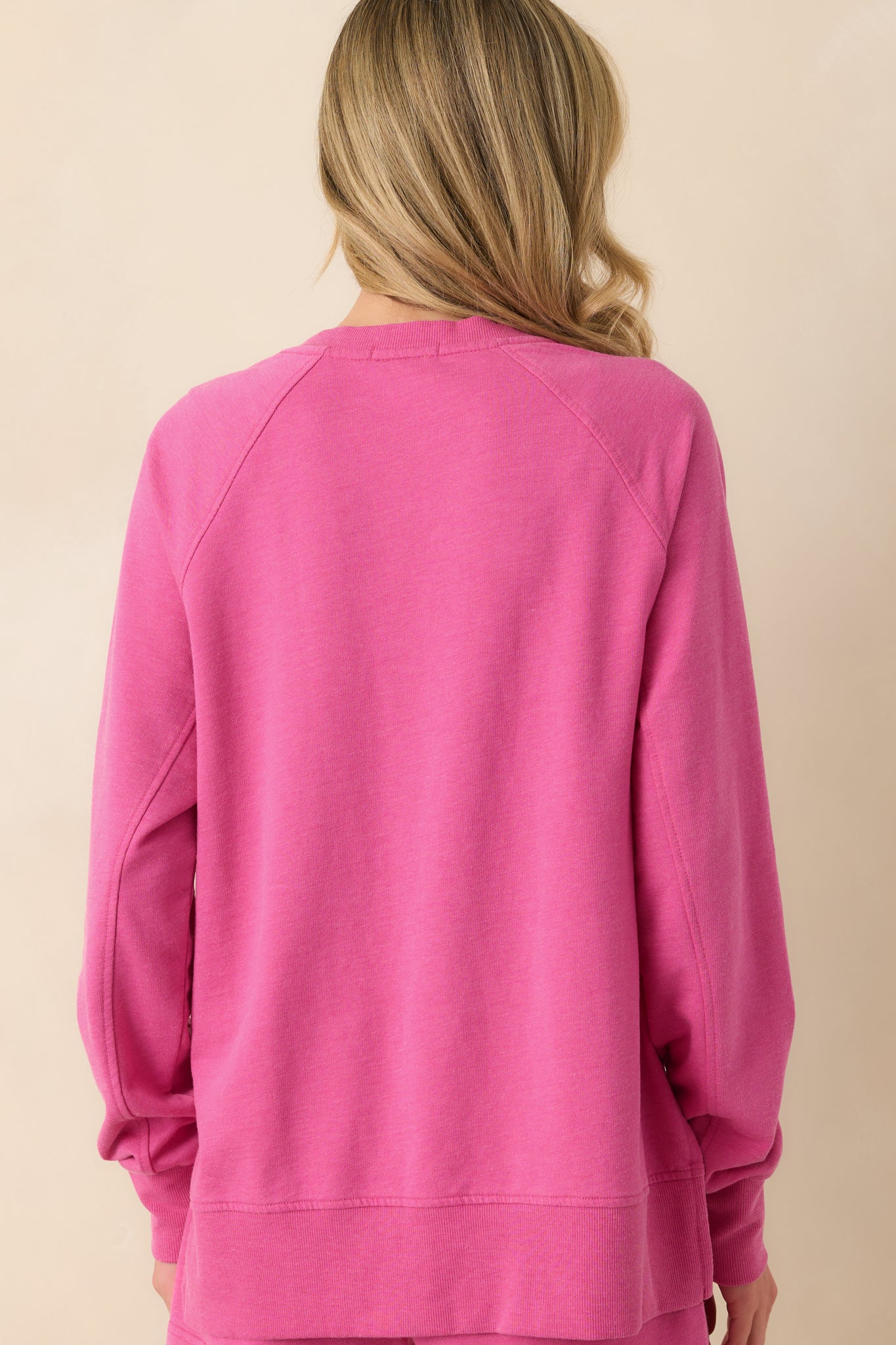 A view from behind of the island pink sweatshirt showing the long sleeves, relaxed fit, and straight back hem with side slits.