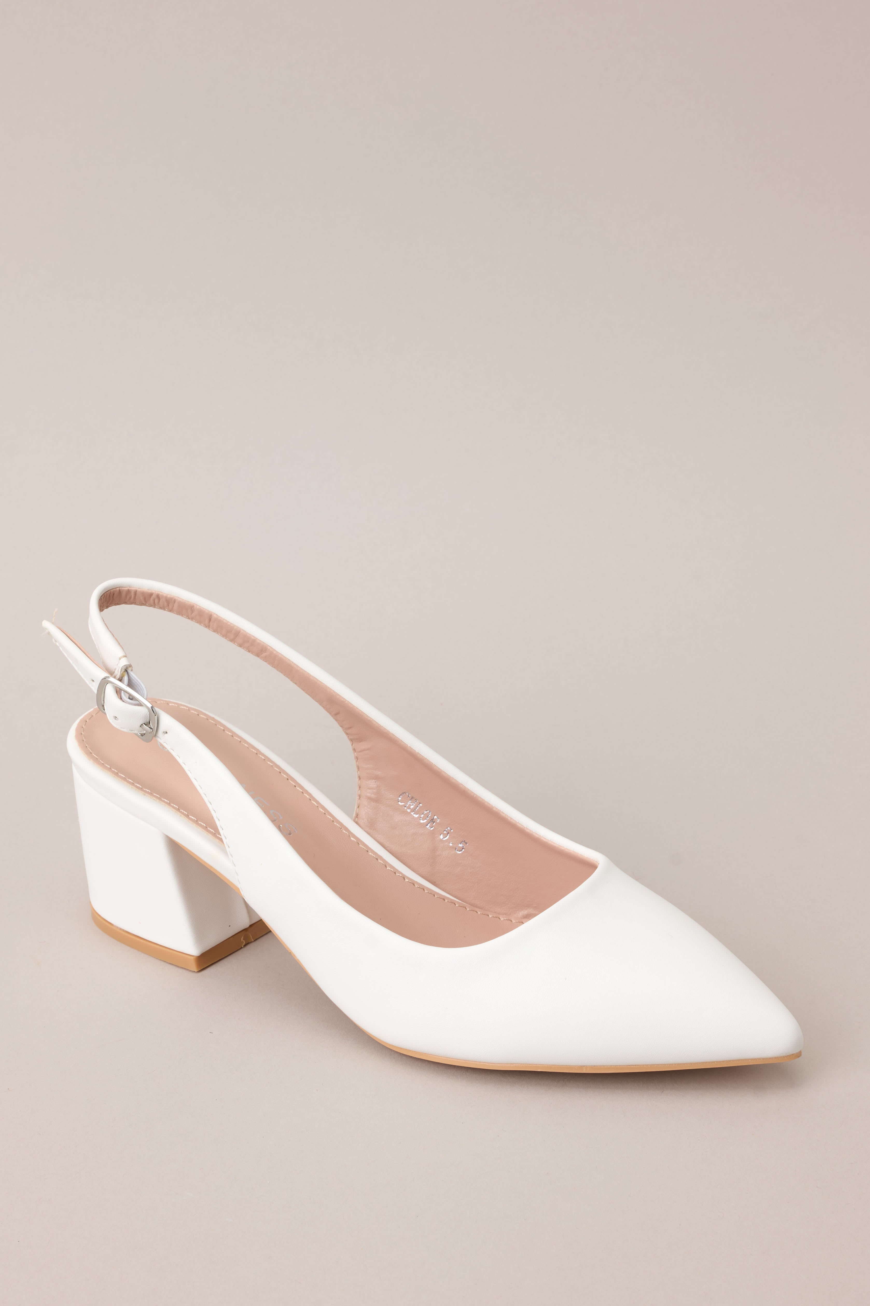 Angled front view of a white heel showcasing its pointed toe, smooth faux leather material, and part of the adjustable strap wrapping around the back.