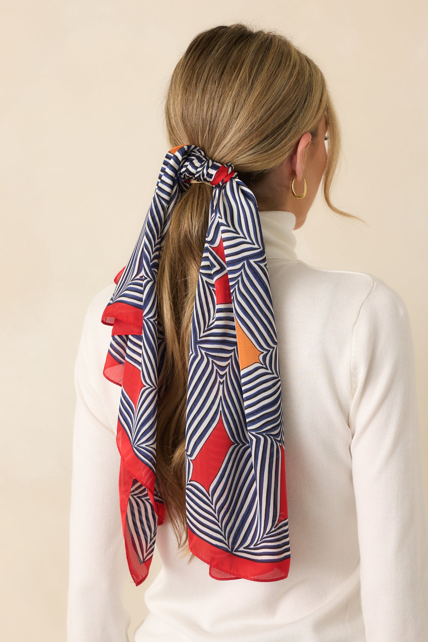 A view from behind showing the red scarf styled in the hair, with the square shape folded to display orange and red color block sections.