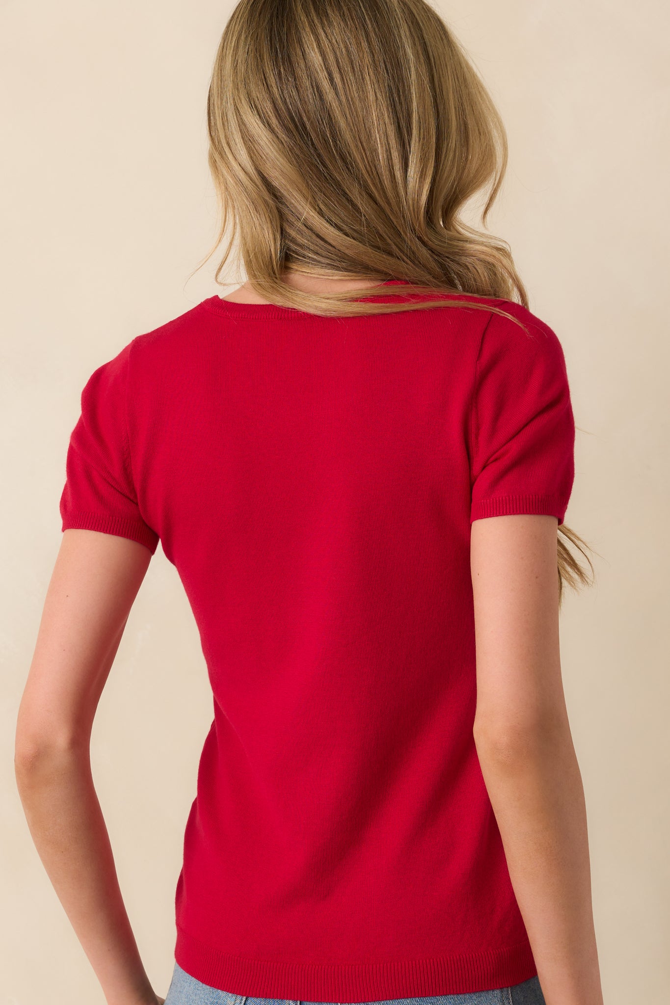 A back view of the red sweater top displaying the short sleeves and consistent ribbed hem finish.