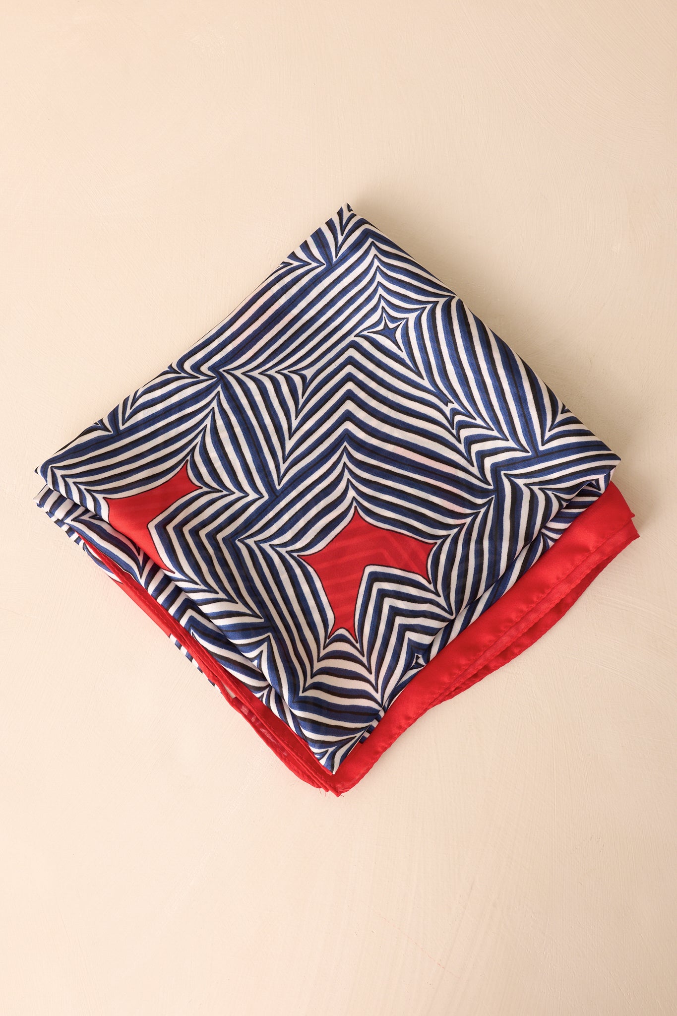 Red scarf neatly folded into a small square, revealing the contrasting orange and red color blocks and stripe patterns along the edges.