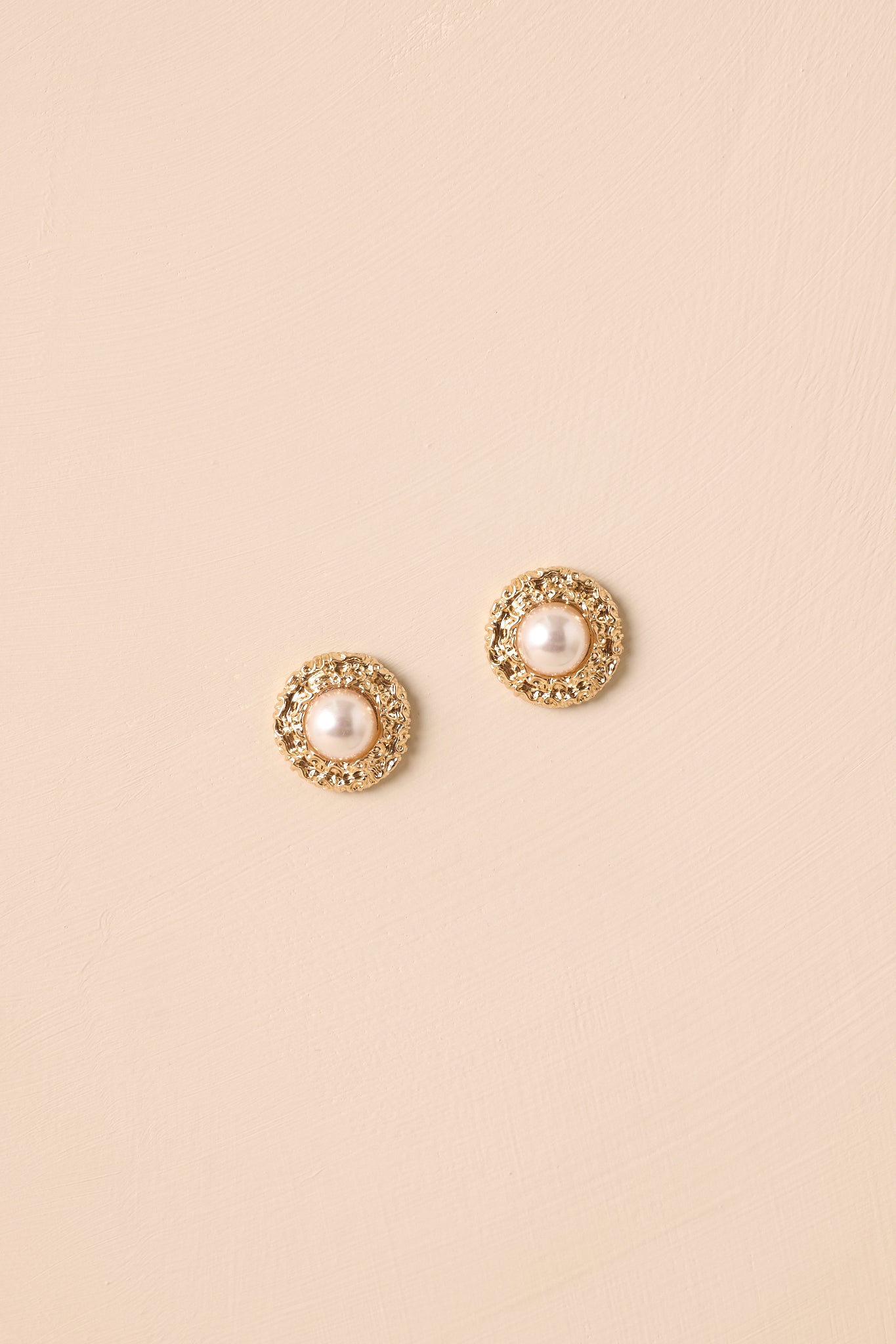 The earrings displayed against a beige background, showcasing the round design and gold detailing.