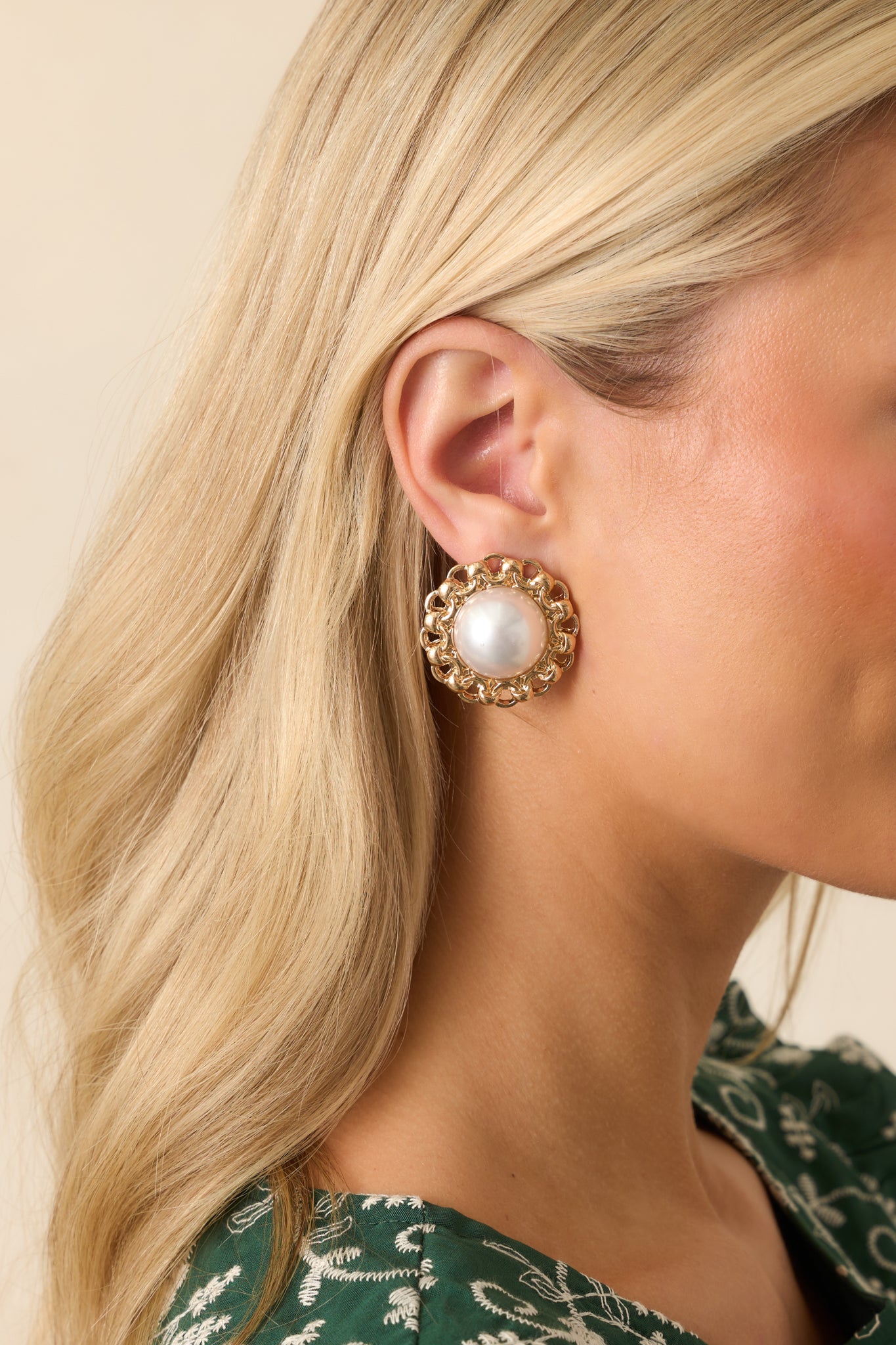 Cropped image showing round ivory faux pearl earrings with decorative gold chain frame.