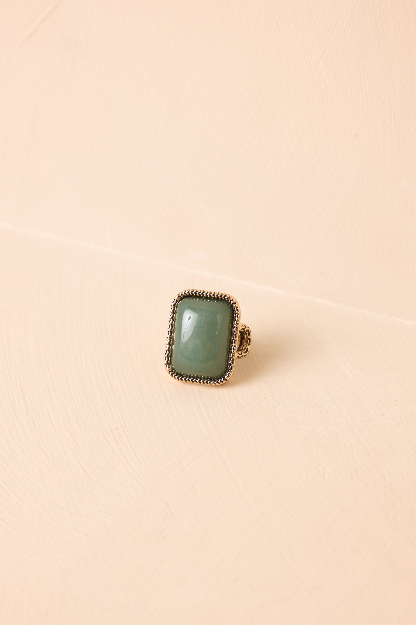 Sage green rectangular statement stone ring with an antique gold adjustable band on a neutral background.