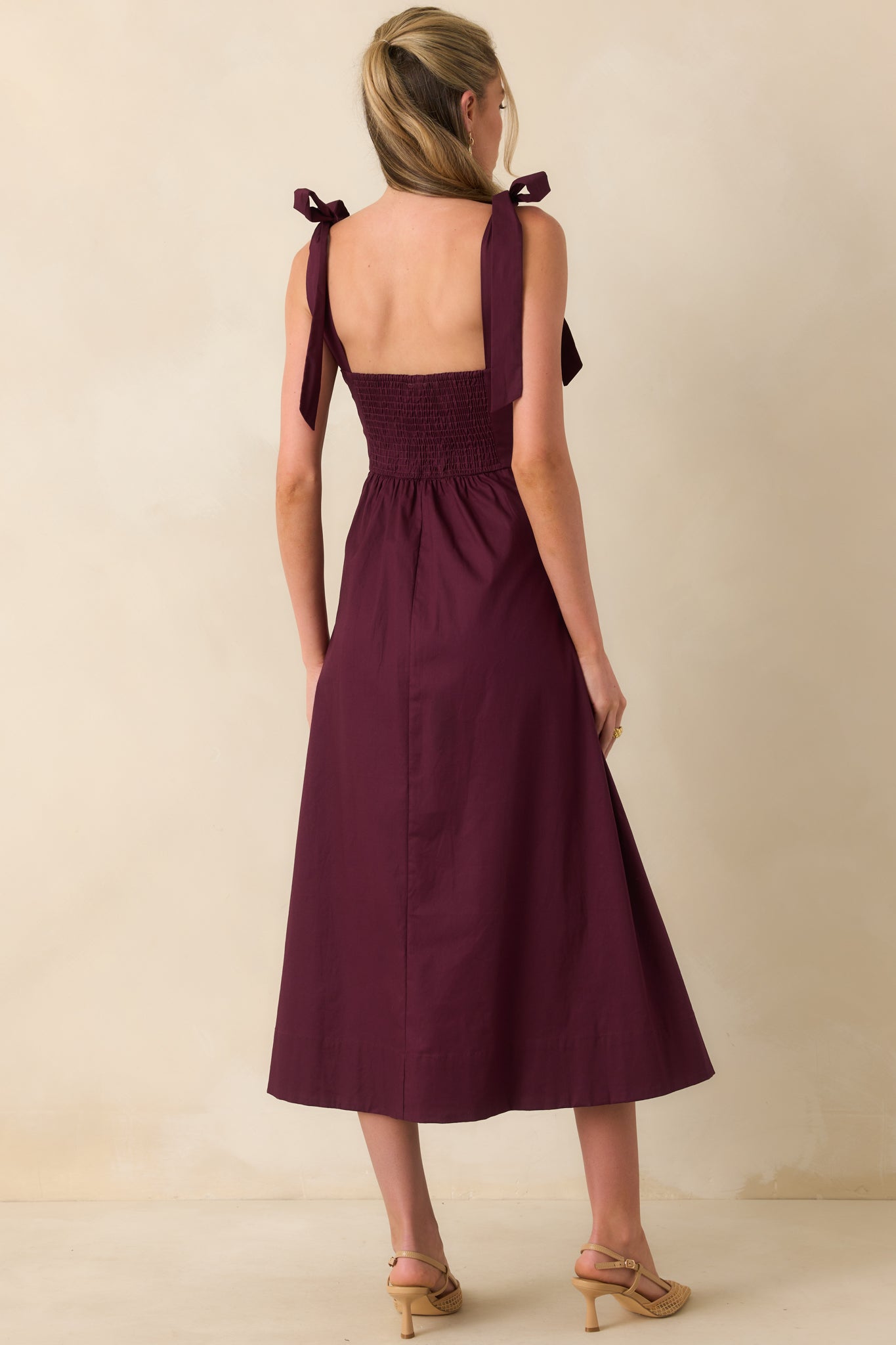 Back view of sangria purple midi dress with smocked panel, adjustable tie straps, and drop waist pleated skirt.