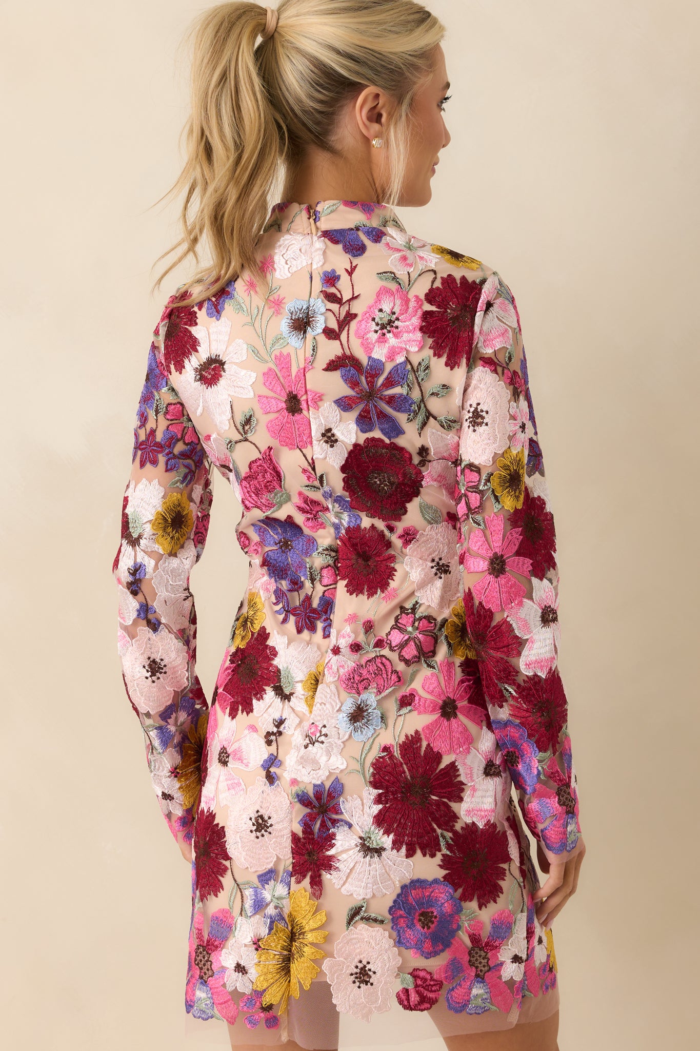 This dress features a high neckline, fitted design, sheer floral overlay, mini length, discrete back zipper and sheer long sleeves.