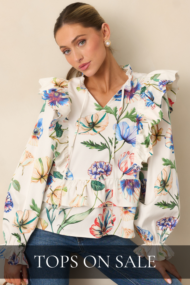 Shop tops on sale featuring a white floral ruffle blouse styled with denim jeans.