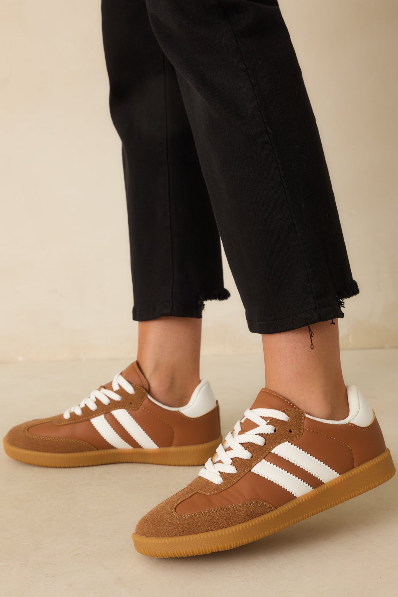 A side shot of the caramel brown low-top sneakers with white side stripes and lace-up design.