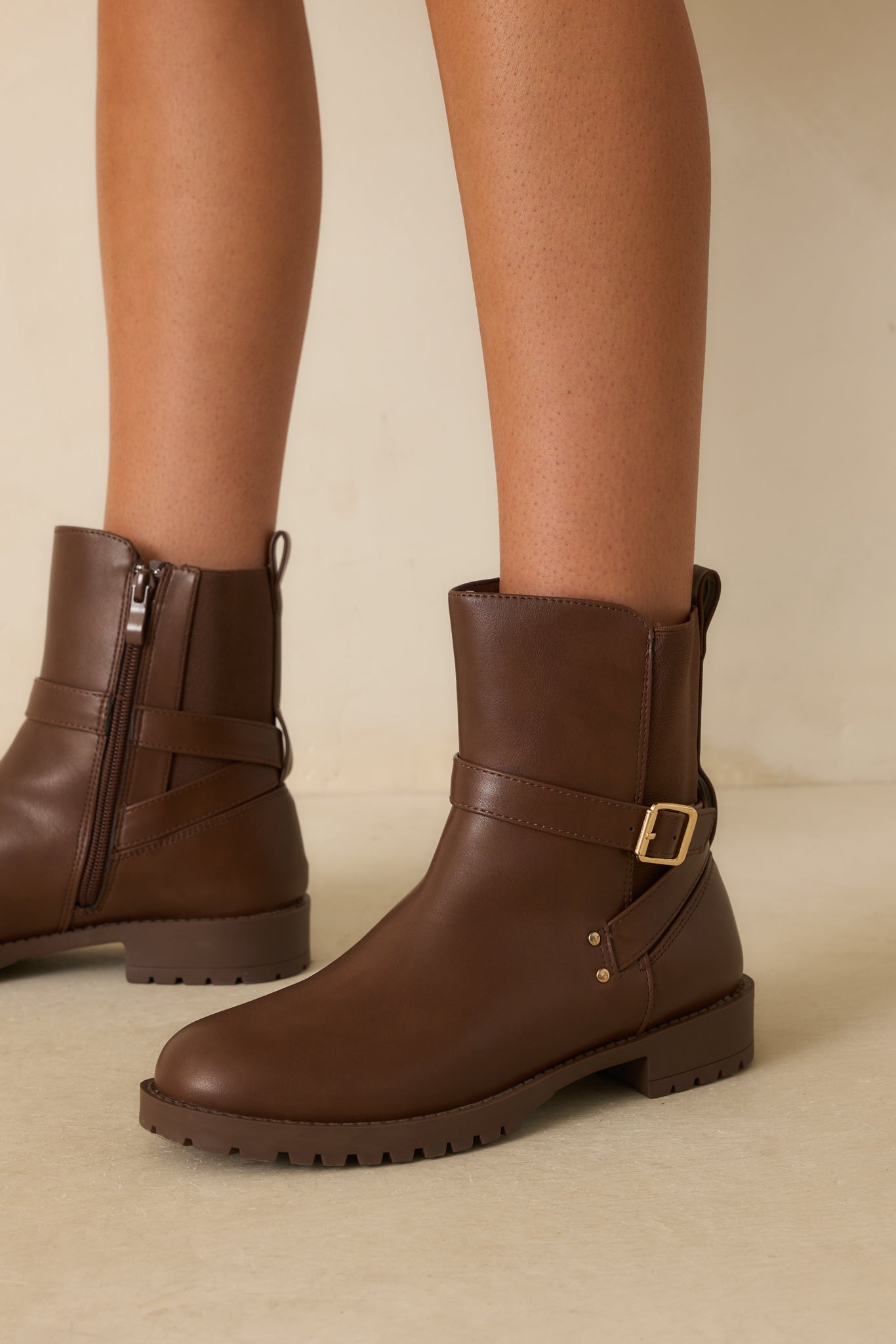 Side view of the chocolate brown ankle boots on beige, highlighting the wraparound strap and side zipper.