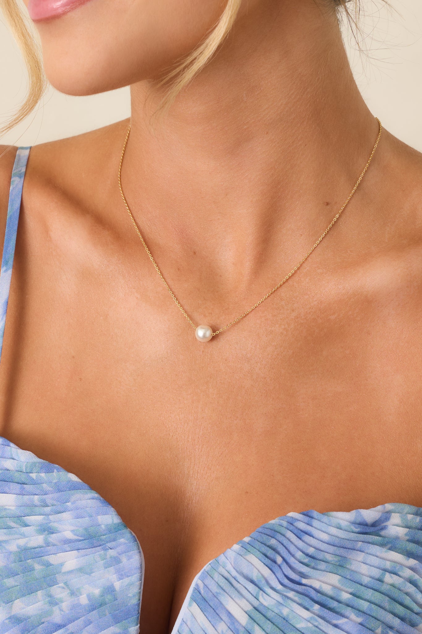 Angled close-up of the Simply The One Pearl Gold Solitaire Necklace with a single pearl pendant on a delicate gold chain worn at the collarbone.