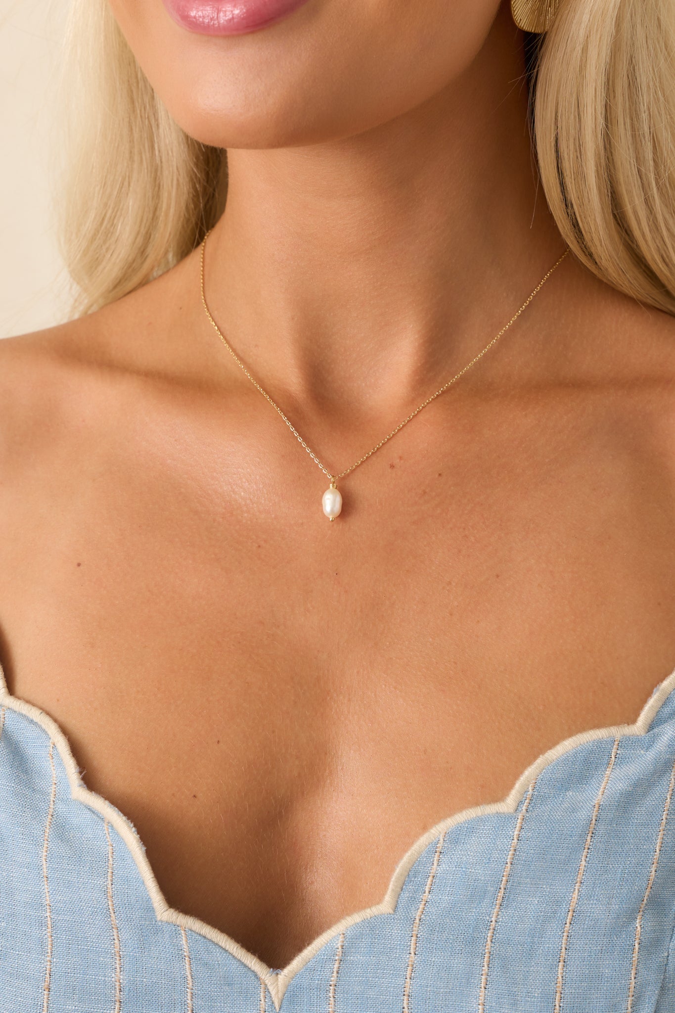 A cropped view of the gold chain necklace draped across the collar area, highlighting the organic-shaped ivory faux pearl charm.