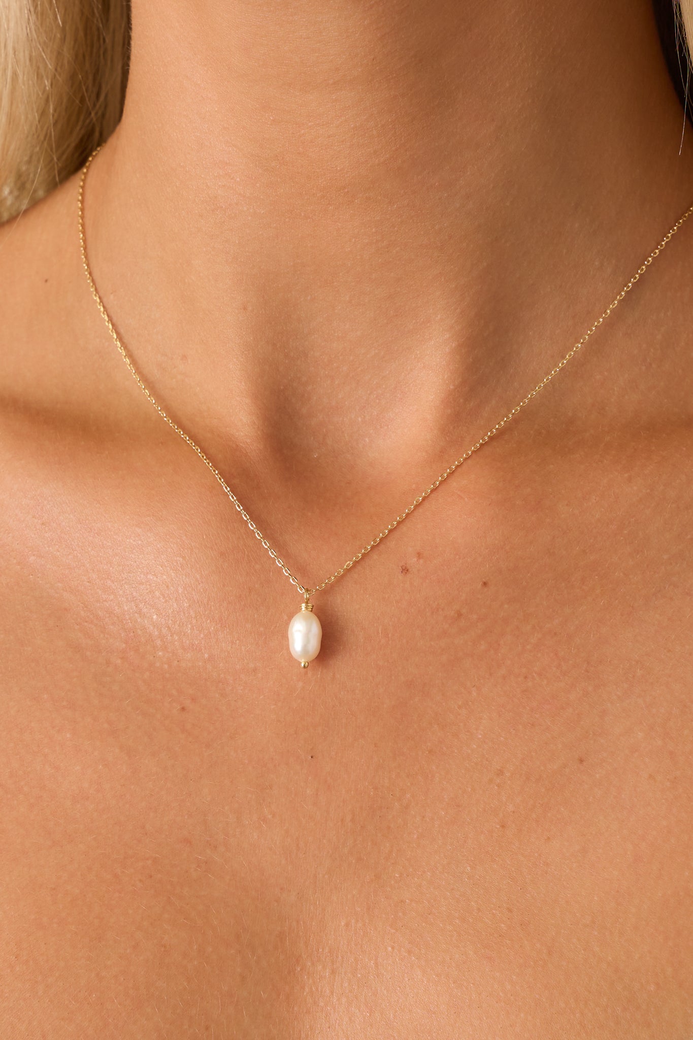 A close-up of the faux pearl charm revealing its organic shape and glossy finish attached to the dainty gold chain.